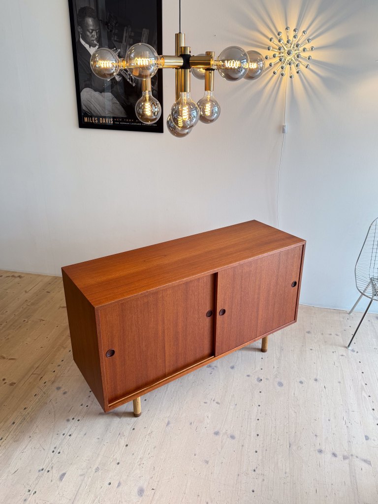 A modern wooden sideboard with two sliding doors and golden legs, placed in a well-lit room featuring decorative light fixtures and a framed black and white poster on the wall.