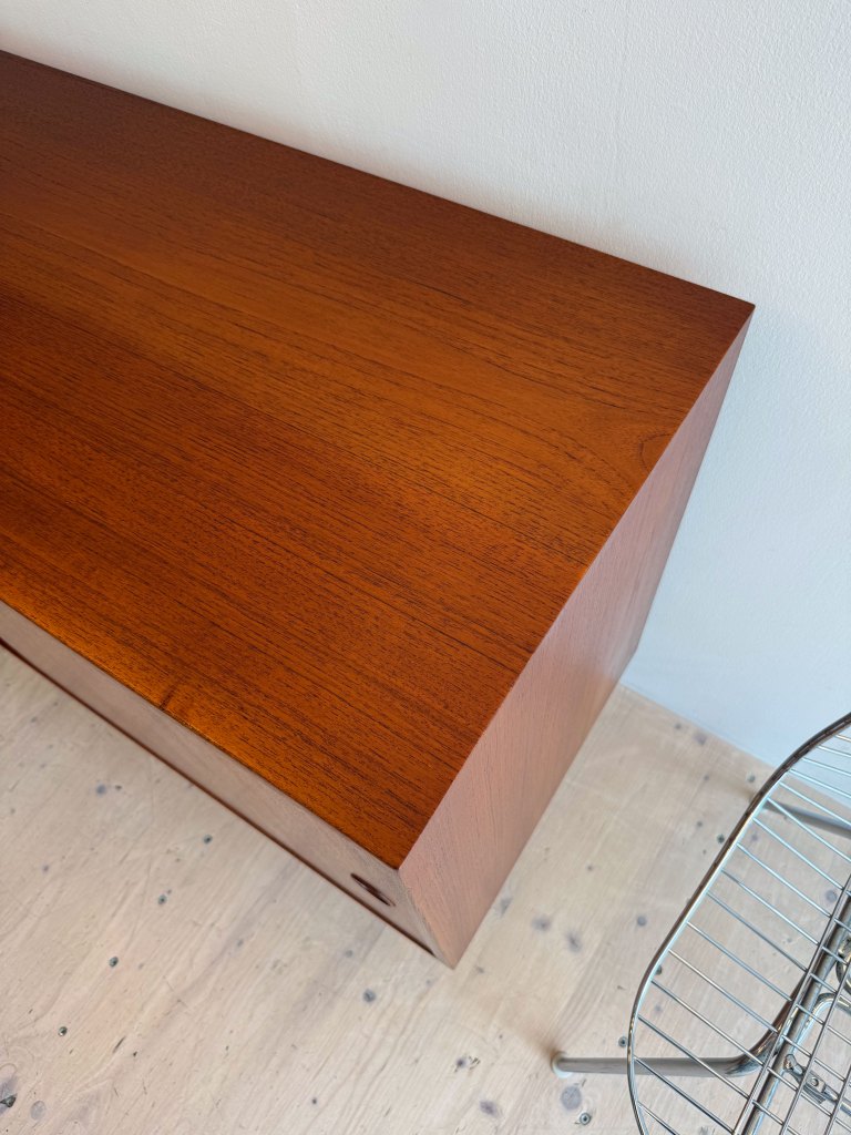 Close-up view of a polished wooden surface with a rich, dark finish, showing the texture and grain pattern, next to a wire chair on a light wooden floor.