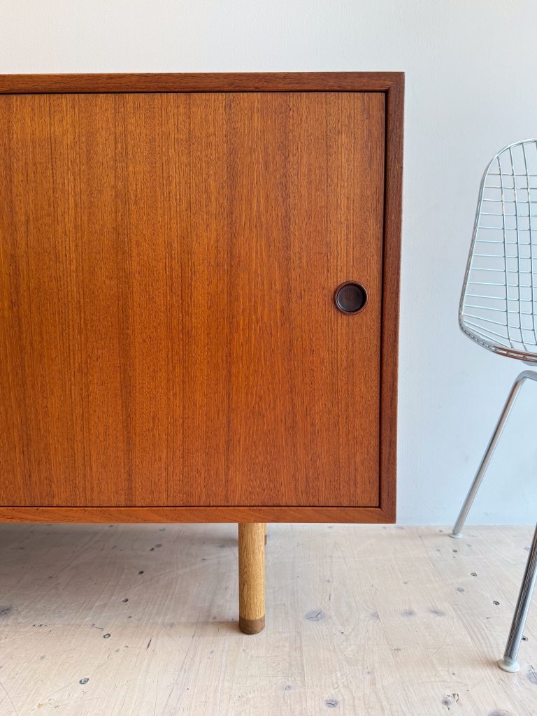 Close-up view of a wooden cabinet with a round handle, paired with a modern wire chair in the background.