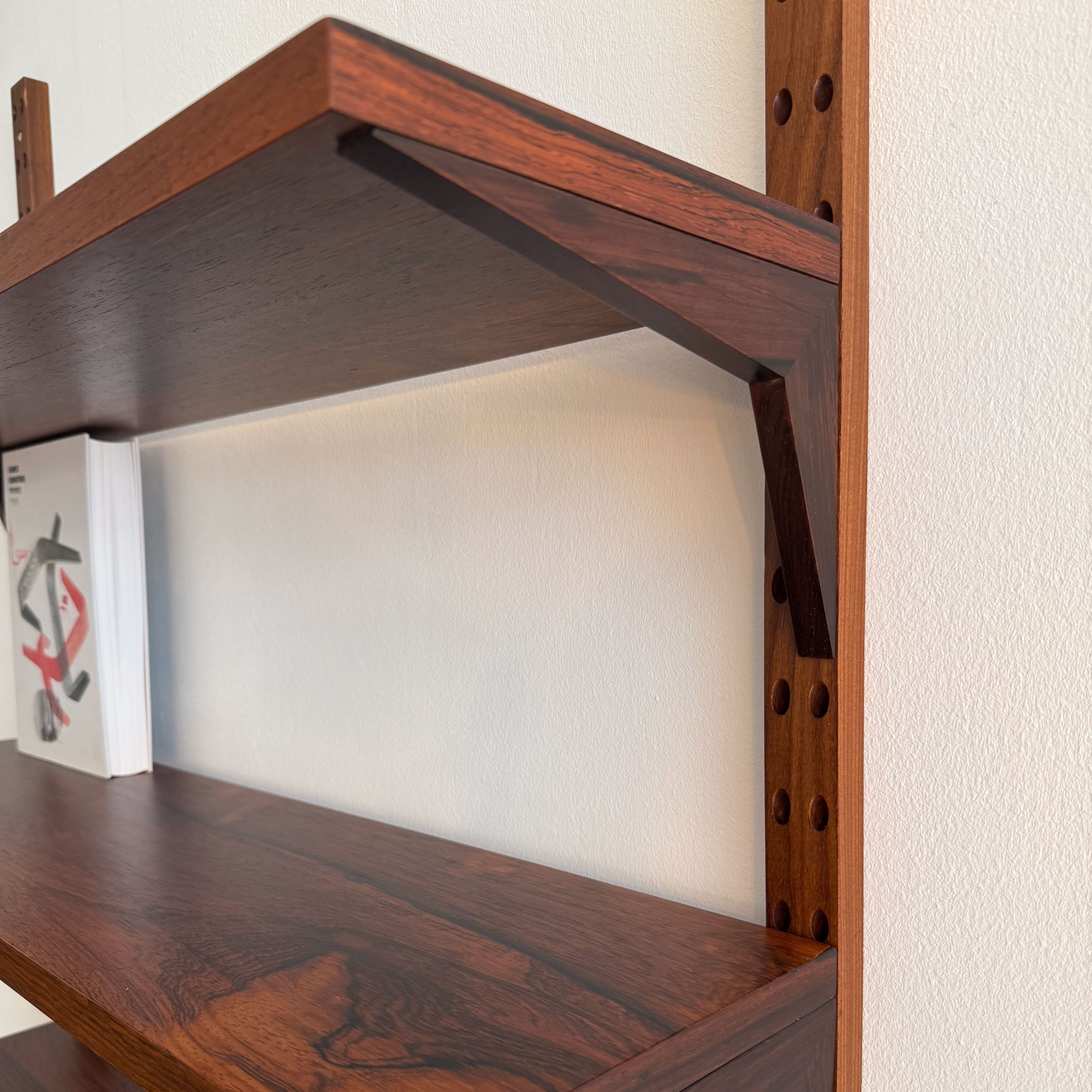 Close-up of a wooden shelf with a rich grain, featuring a slim design and decorative wooden brackets, mounted on a wall.