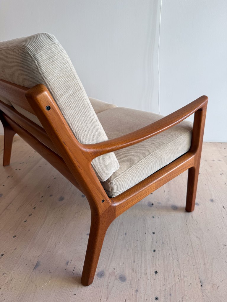 A close-up view of a mid-century modern chair featuring a wooden frame and beige fabric upholstery.