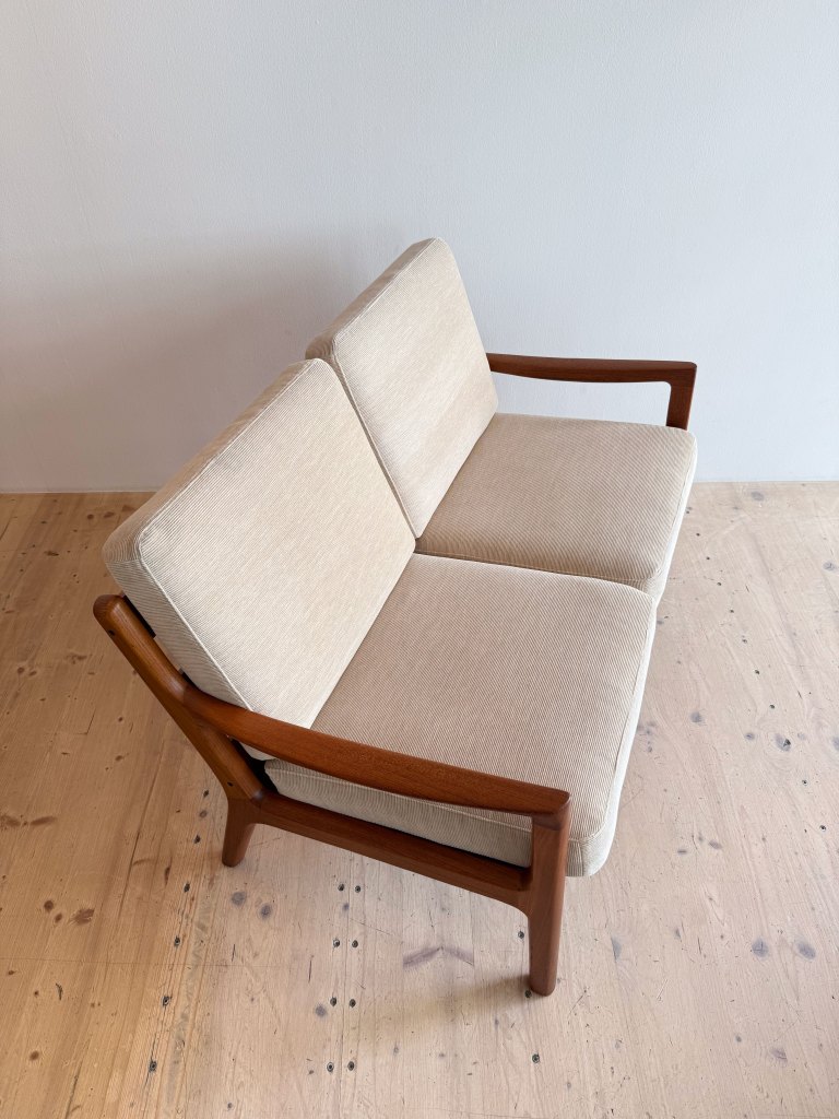 A stylish two-seater sofa with a light beige fabric and wooden frame, set against a neutral background.