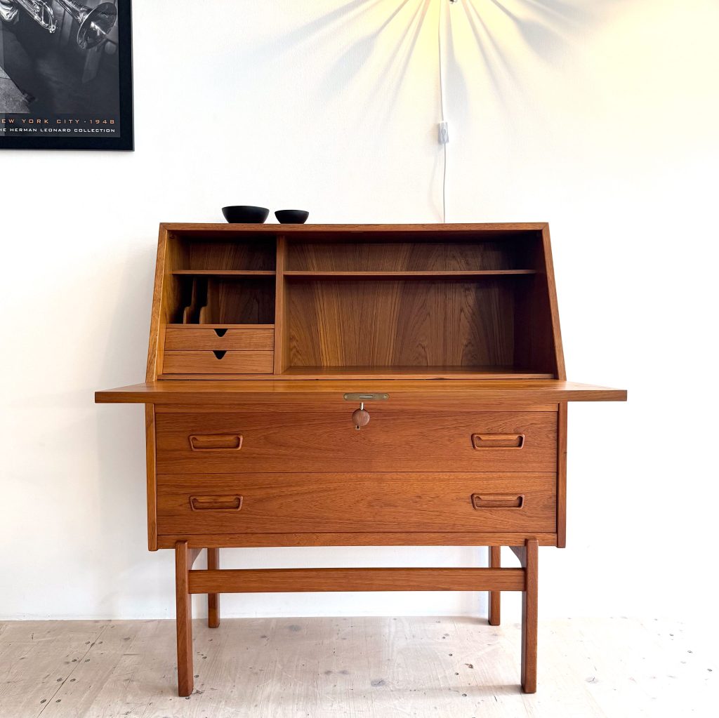 Mid-century modern wooden desk with a hutch, featuring open shelves and drawers, placed against a white wall.