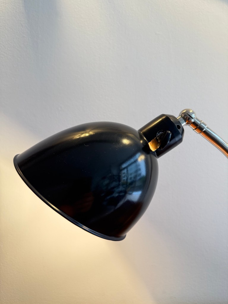 A close-up view of a vintage Bauhaus desk lamp with a black dome shade, showcasing its industrial design and clean lines.