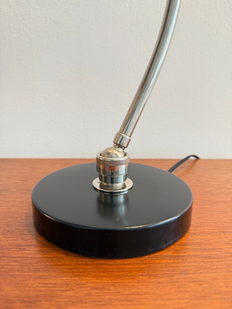 A close-up view of the base of a Bauhaus desk lamp, featuring a sleek black circular base and a shiny metallic socket.