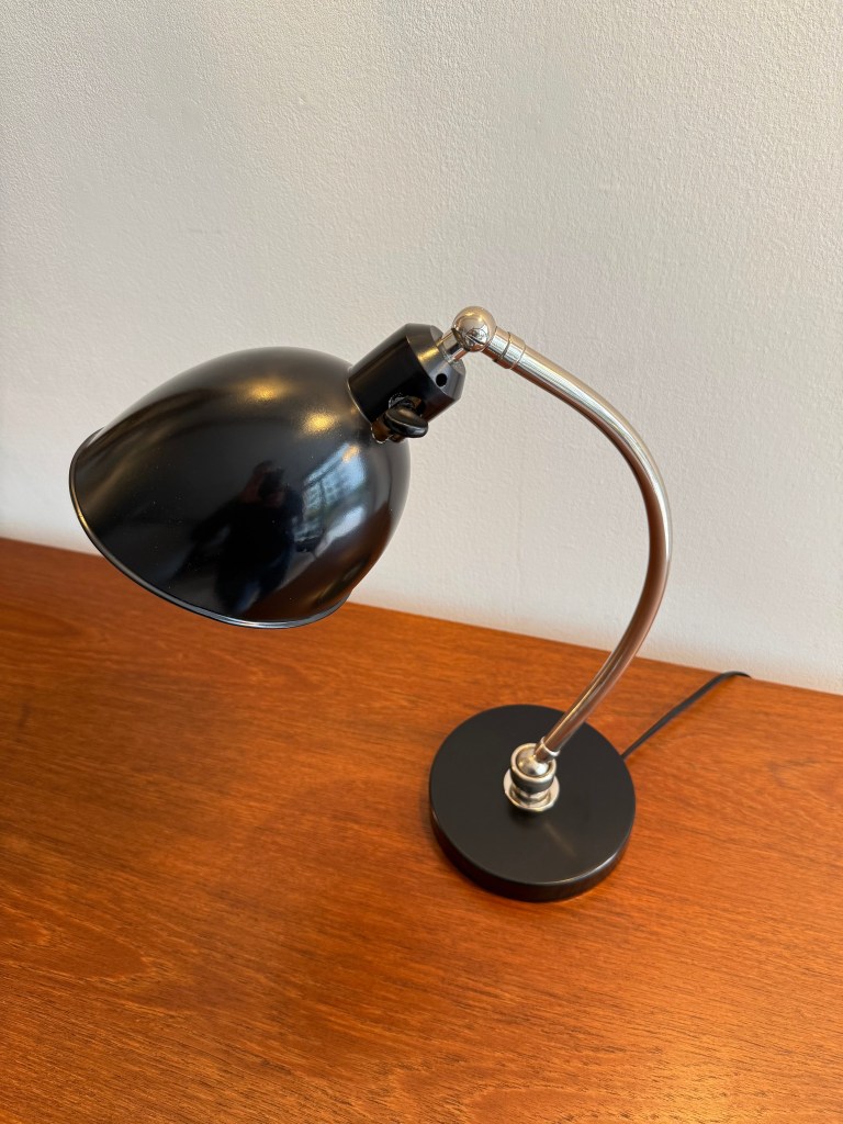 Bauhaus desk lamp with a black shade and a curved metal arm, placed on a wooden surface.