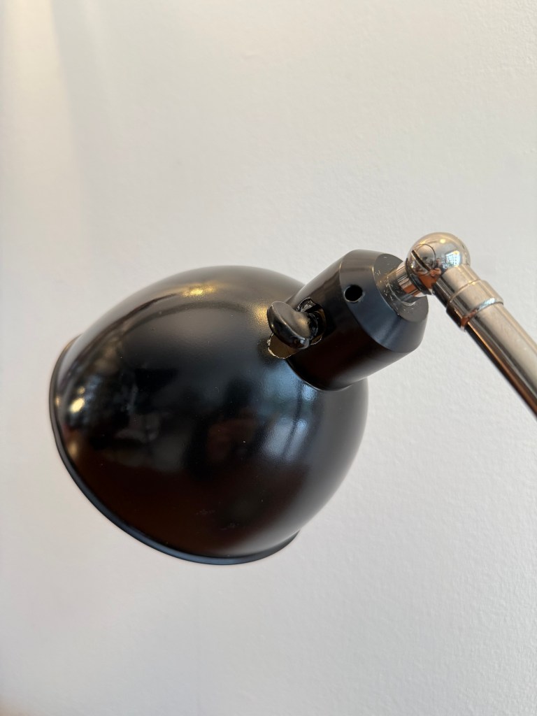 Close-up of a Bauhaus desk lamp with a black shade and metallic arm, highlighting its industrial design.