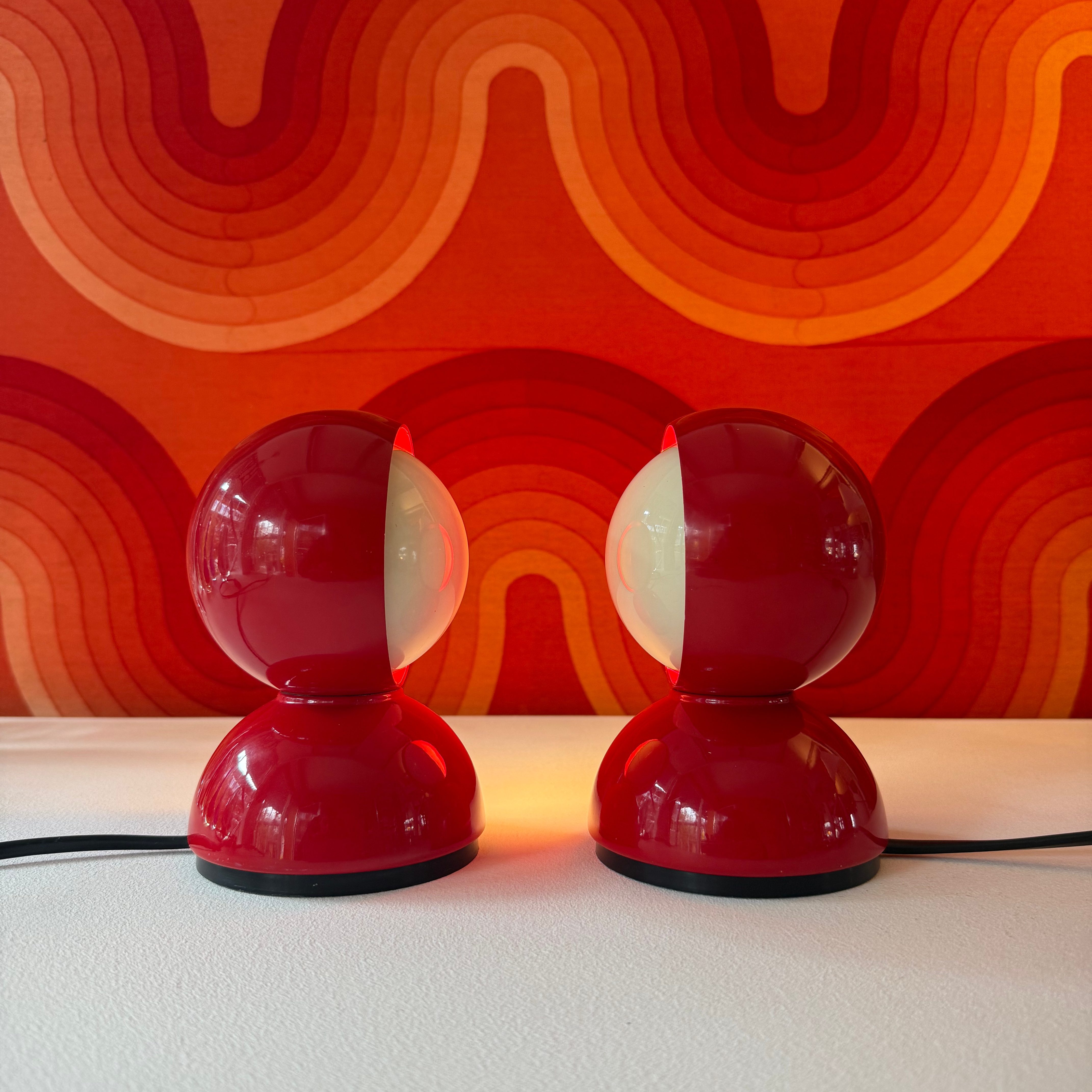 Pair of retro red table lamps with round bases and light spheres, set against a colorful wave-patterned background.
