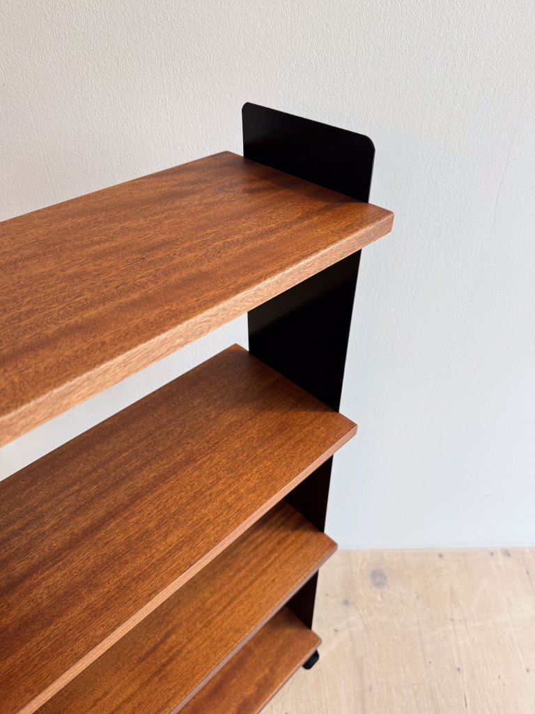 Close-up view of a wooden shelf with a rich mahogany finish, featuring a black metal support on one side, against a neutral wall.