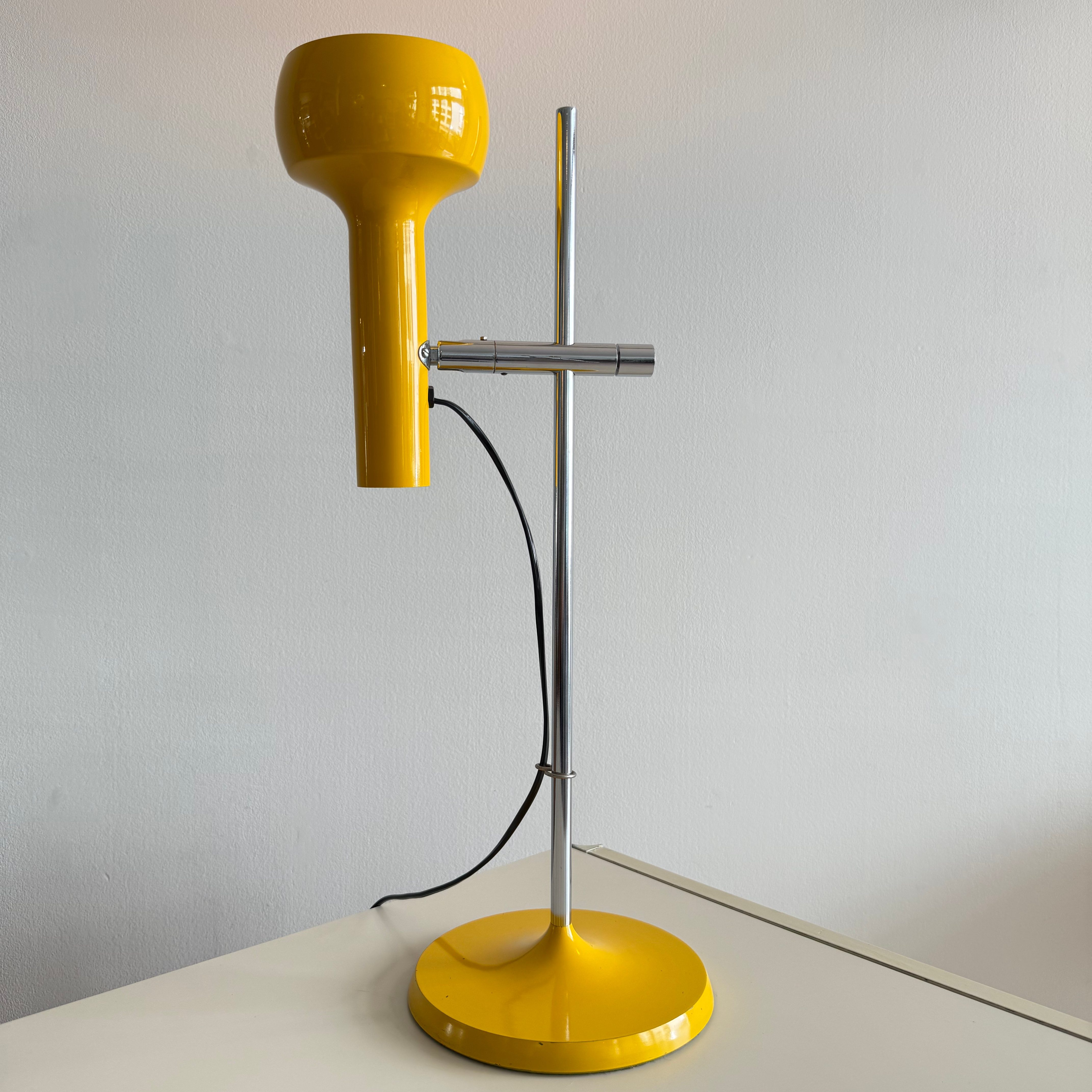 A modern yellow desk lamp with a chrome stand, featuring a round base and a bulbous shade.