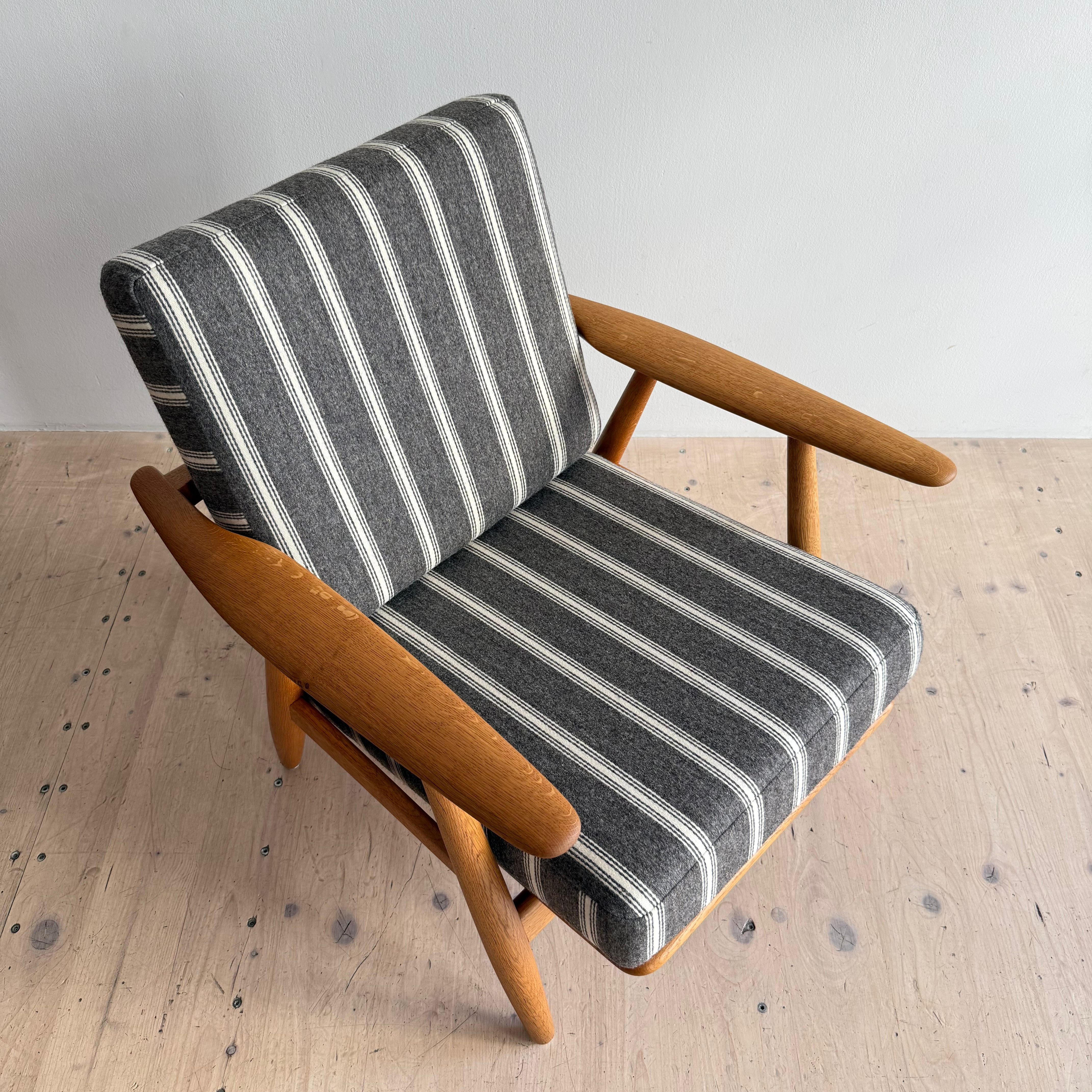 A striped lounge chair with wooden arms and legs, positioned on a light wooden floor.