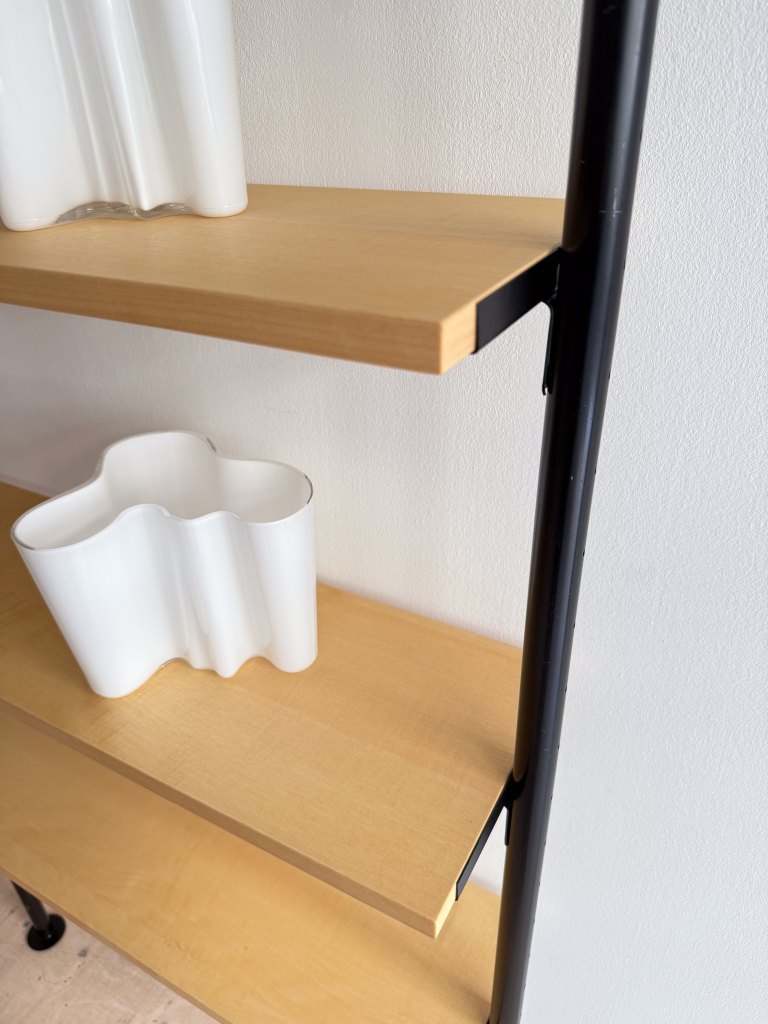 Close-up of a wooden shelf featuring two decorative white vases, one with a wavy design, against a plain wall.