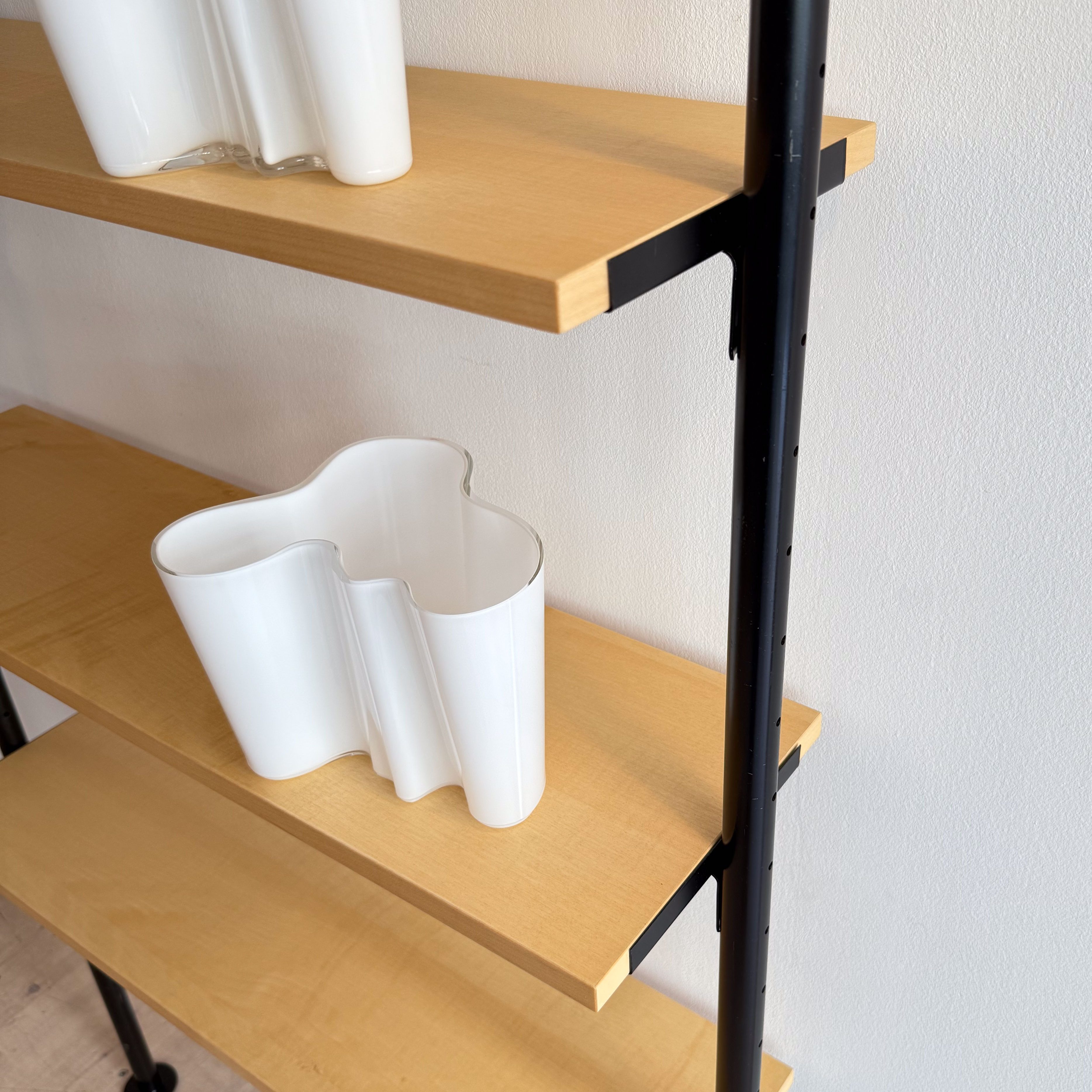 Close-up of a wooden shelf unit featuring two white vases, one with a wavy design, on a smooth wooden surface.