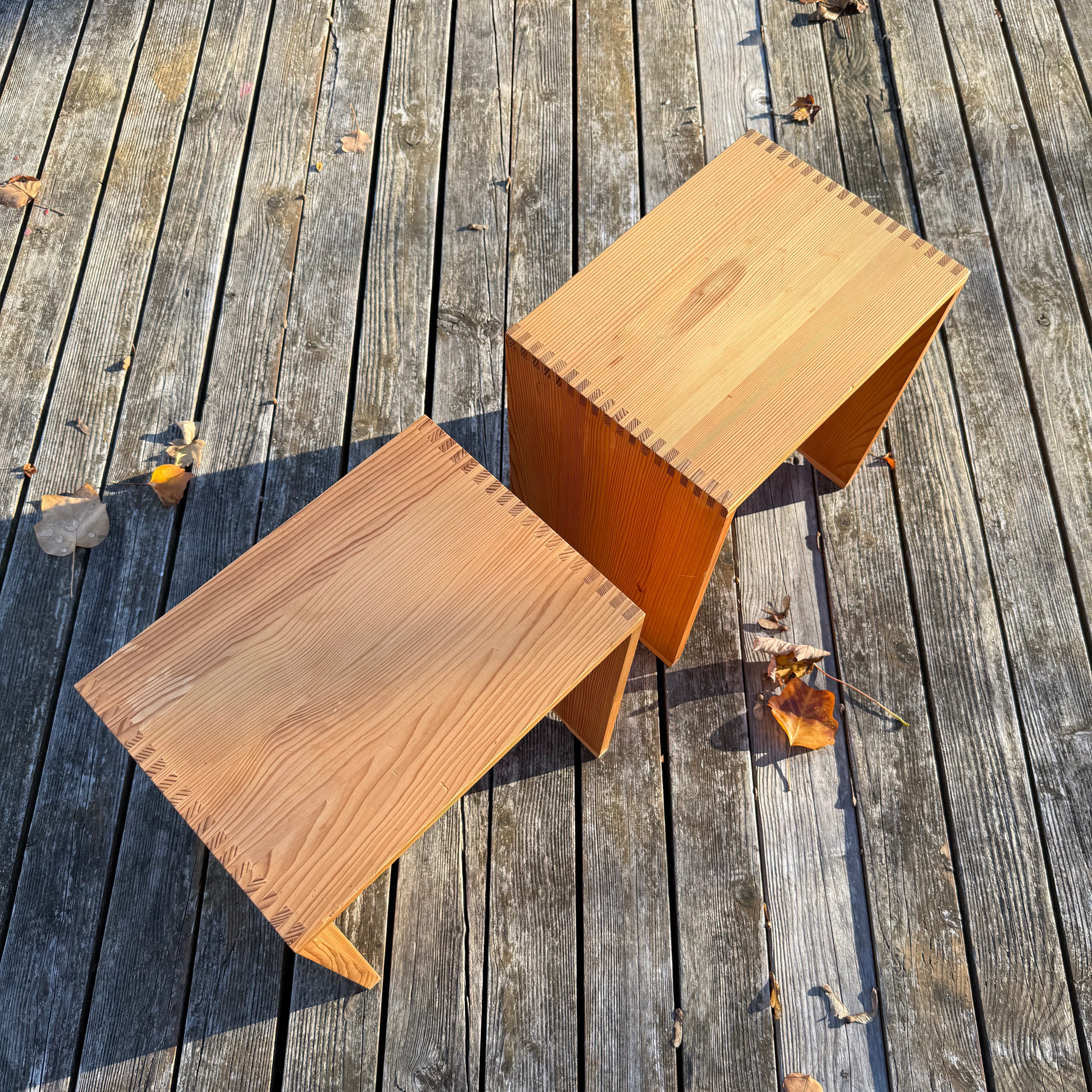 Two wooden side tables made of light-colored wood, displayed on a wooden deck with autumn leaves.