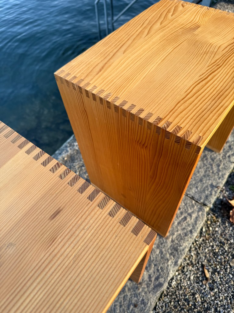 Close-up of two wooden furniture pieces with a joinery detail, positioned near water.