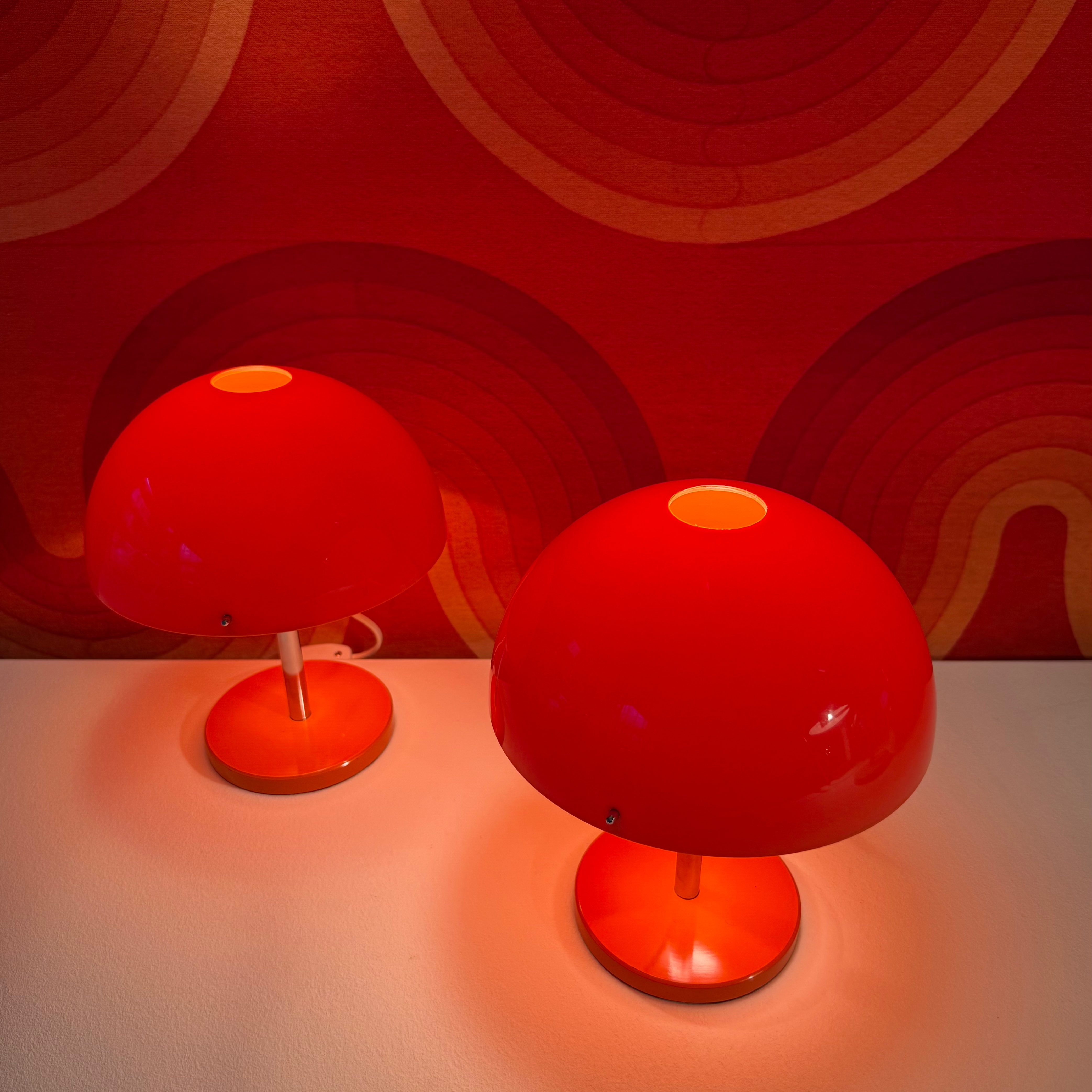 Two red table lamps with spherical shades, placed on a white surface against a vibrant red patterned background.