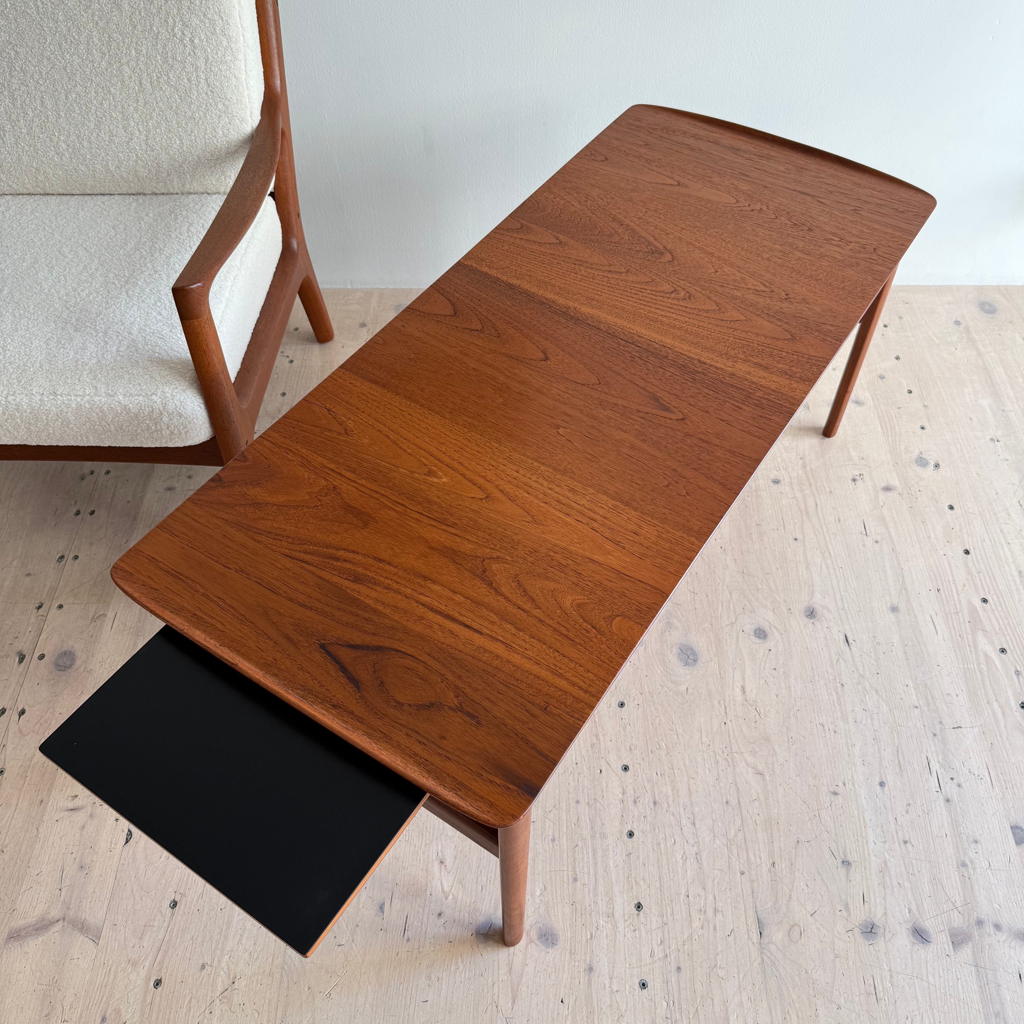 A wooden coffee table with a sleek design, featuring a smooth surface and a black drawer, positioned next to a light-colored armchair.