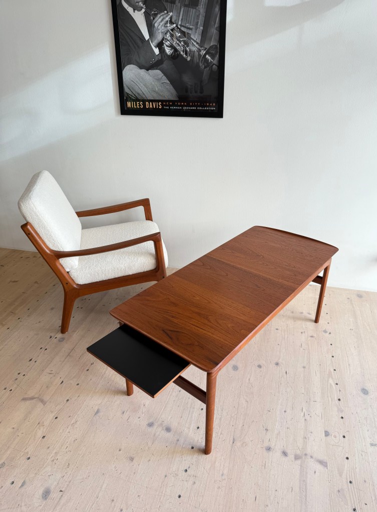 Mid-century modern wooden coffee table with a drawer and an armchair in the background, featuring a classic jazz poster of a musician.