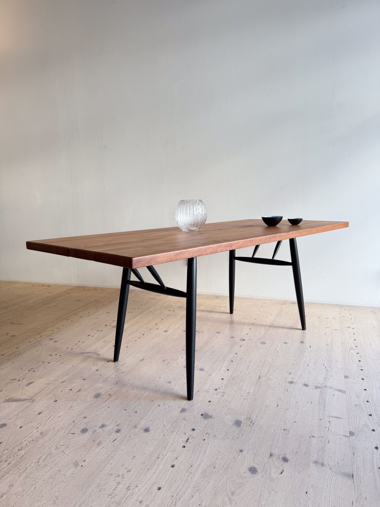 A modern wooden table with a smooth surface and black legs, featuring a decorative glass vase and two small bowls on top.