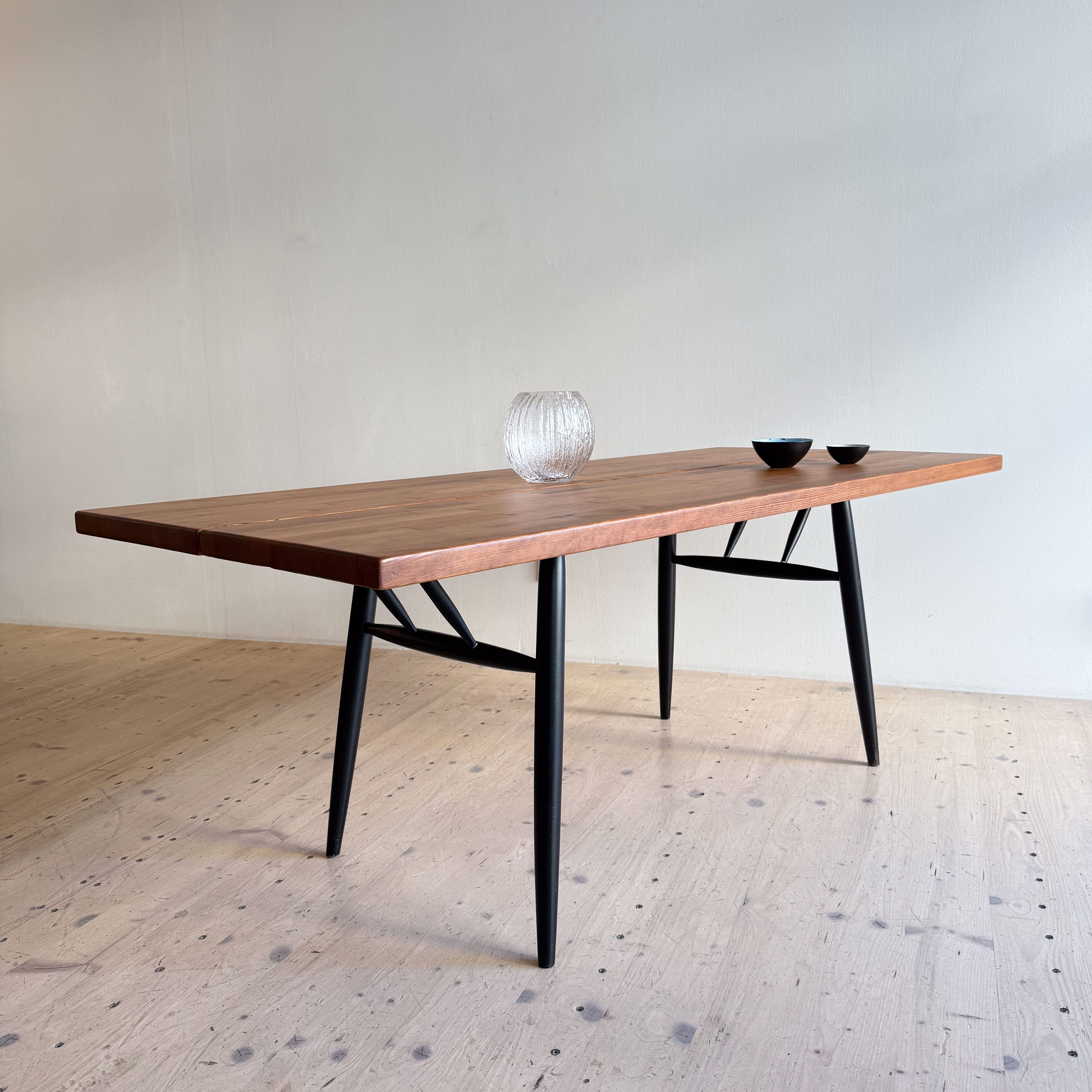 A modern rectangular dining table made of wood with a natural finish, featuring black legs and styled minimalist decor including a glass vase and two bowls.