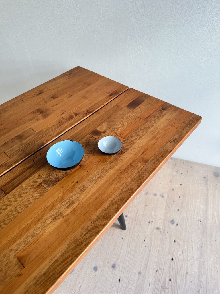A wooden table with two bowls, one large blue bowl and a smaller gray bowl, placed on its surface.