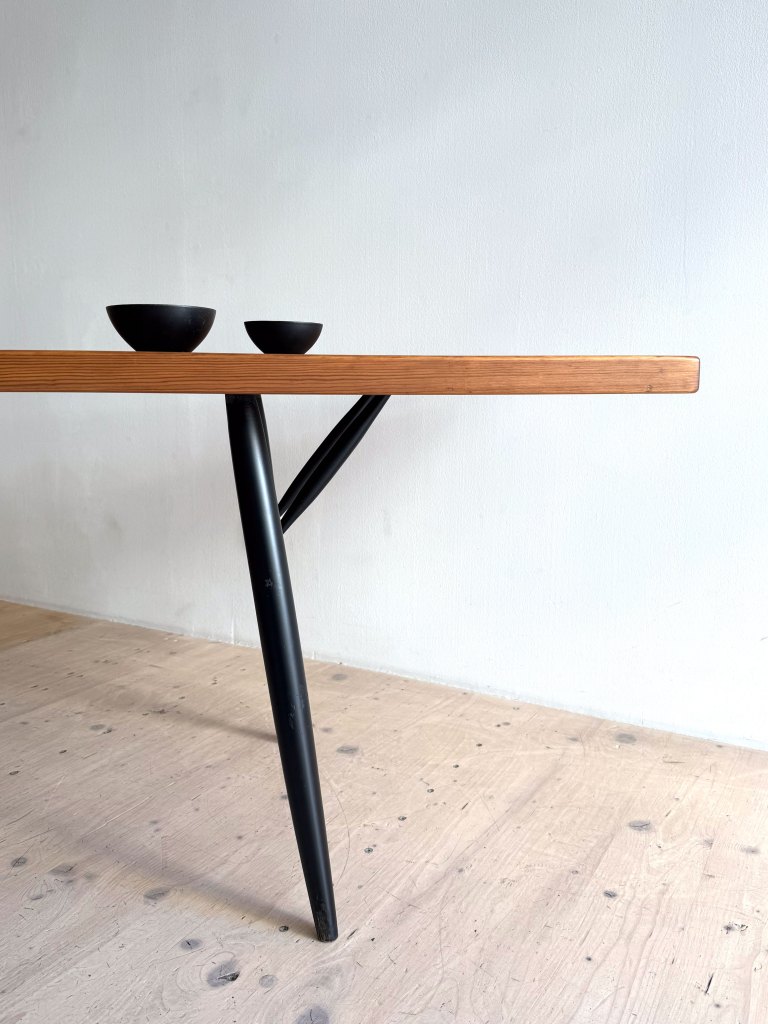 A modern wooden table with a sleek black metal leg design, accompanied by two small black bowls on top.