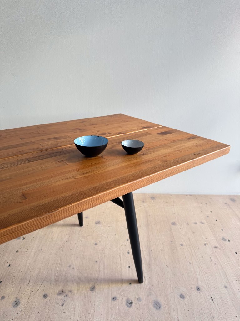 A wooden table with two black bowls on it, set against a plain wall.