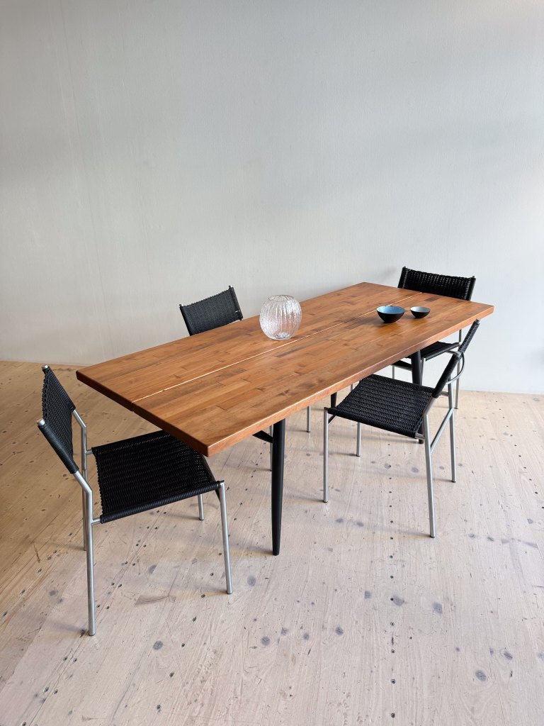 A wooden dining table with four black chairs, featuring a glass vase and two small bowls on the table.