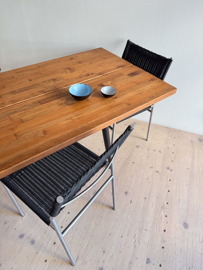 A wooden table with two bowls, one larger black and blue bowl and a smaller white bowl, accompanied by a black woven chair.