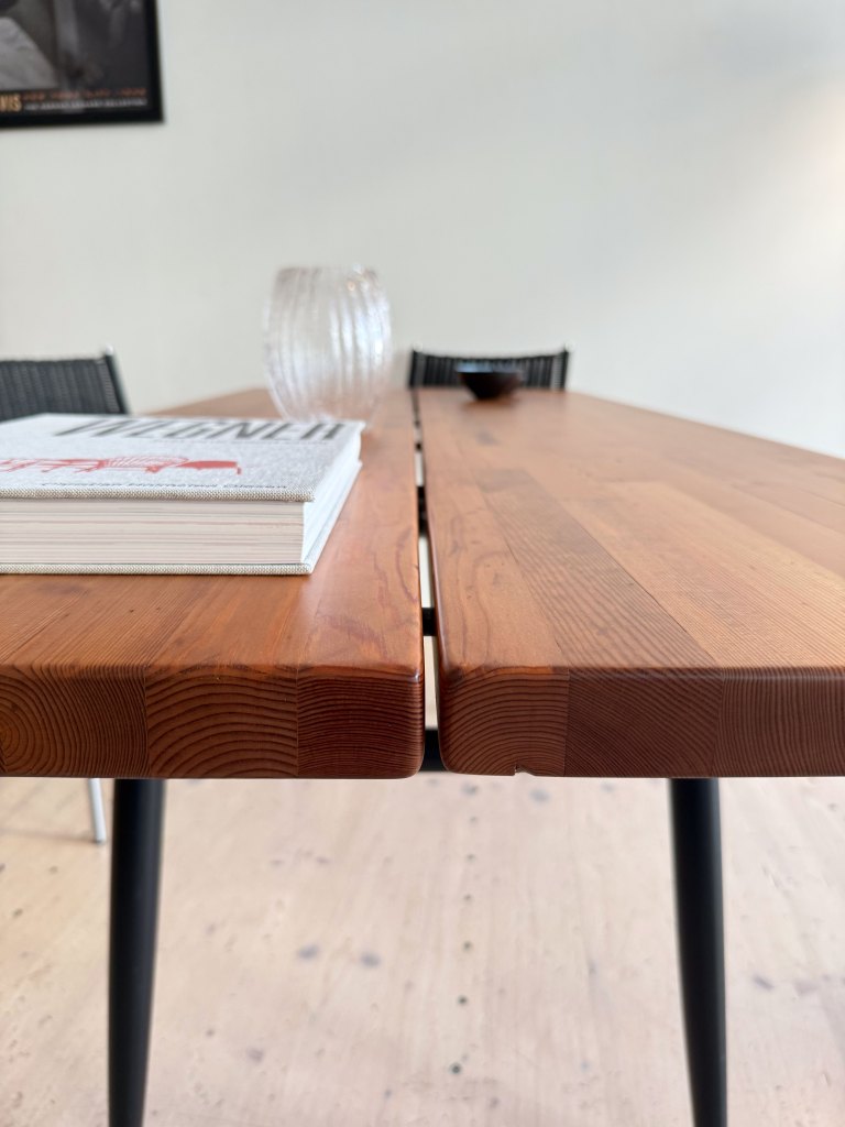 Close-up view of a wooden table with a book, a glass vase, and a small bowl, set against a minimalist backdrop.