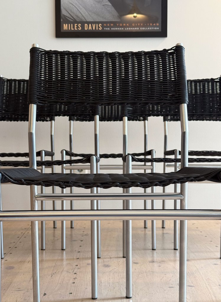 A close-up view of several black woven chairs with metallic legs arranged in a row, showcasing their design and structure.