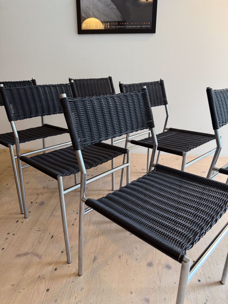 A group of black woven chairs with metal frames arranged in an indoor space, with a poster of Miles Davis on the wall in the background.