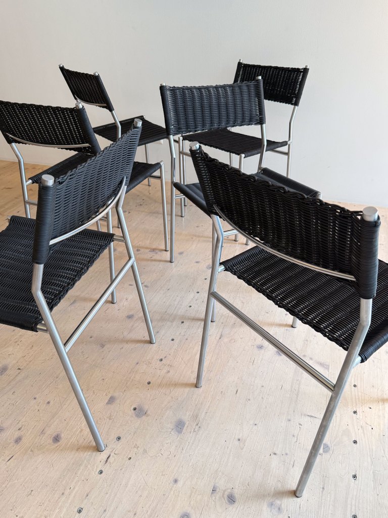 A group of black woven chairs with metallic legs arranged in a casual setting on a wooden floor.