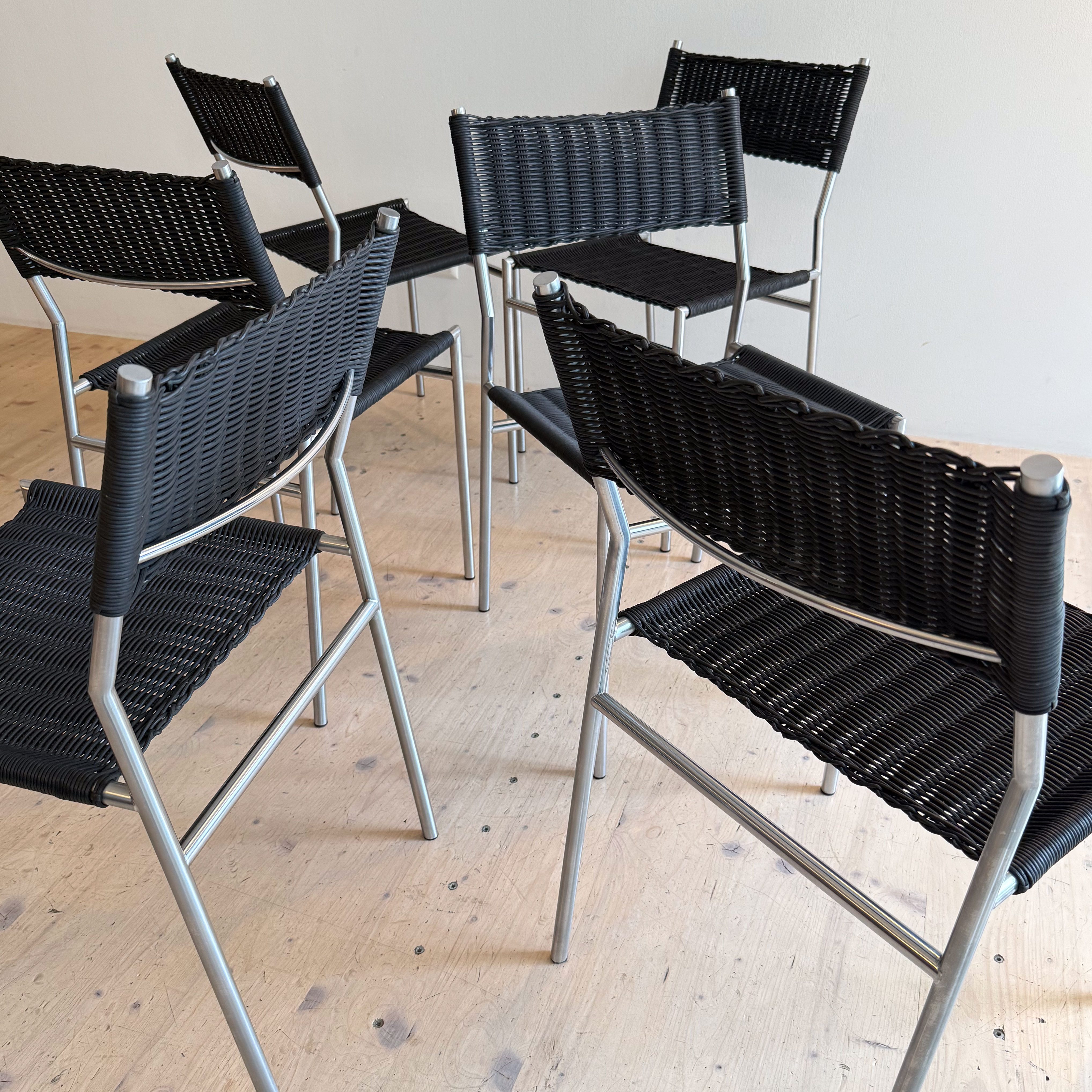 A close-up view of several black wicker dining chairs arranged on a wooden floor.