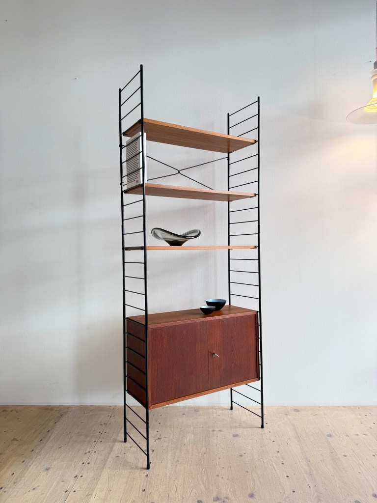 A modern bookshelf with black metal frame and wooden shelves, featuring a lower cabinet with sliding doors and decorative items on top.