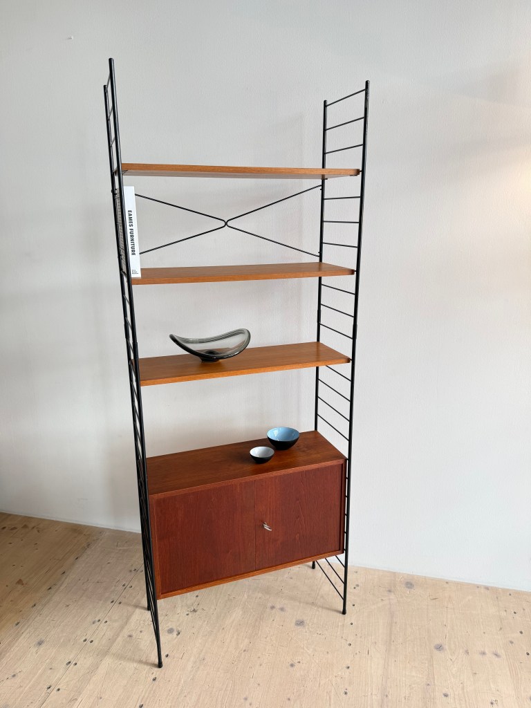 A modern bookshelf with wooden shelves and a dark metal frame, featuring a closed cabinet section at the bottom and decorative bowls on the shelves.