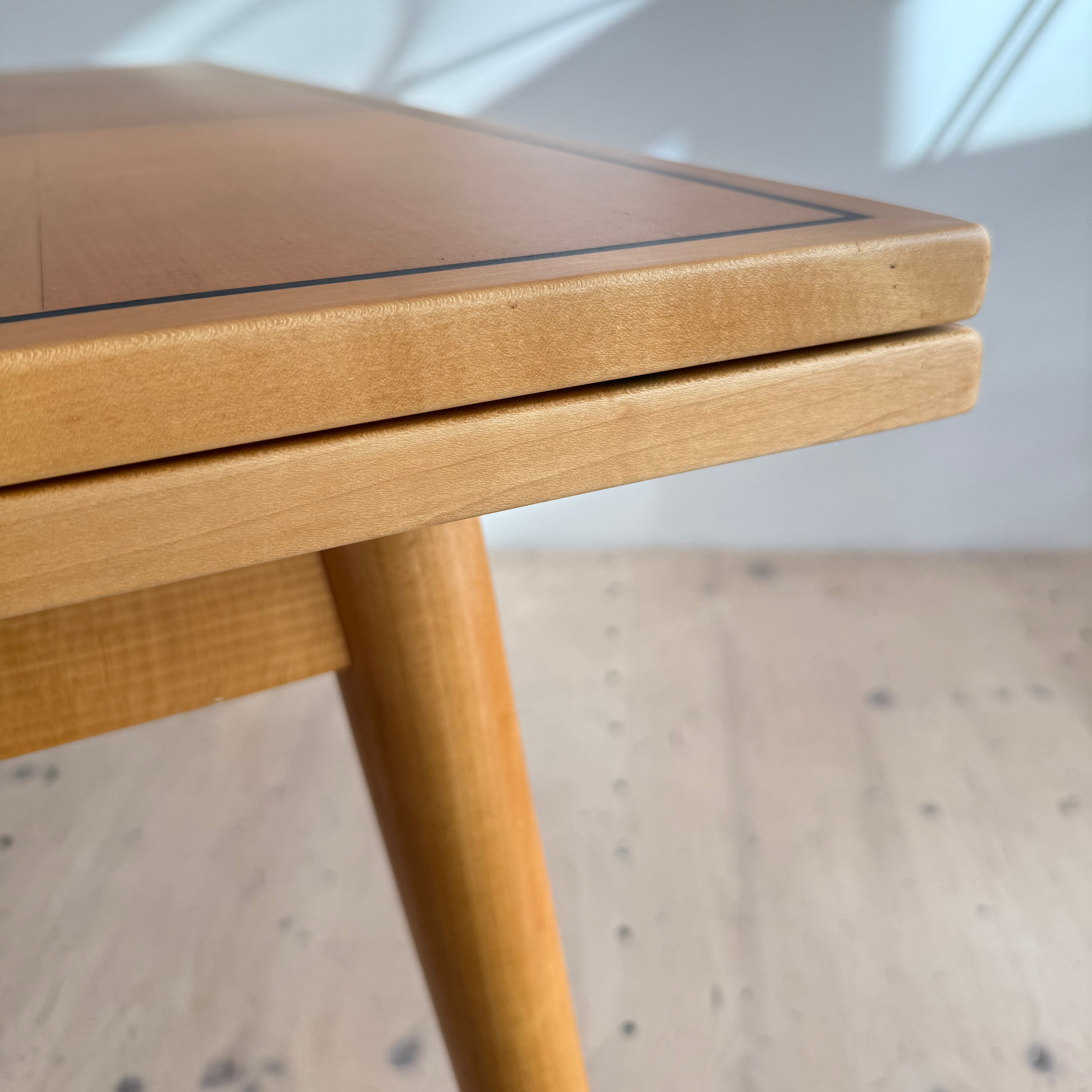 Close-up view of the corner of a wooden table, showcasing its smooth surface, polished edge, and tapered legs.