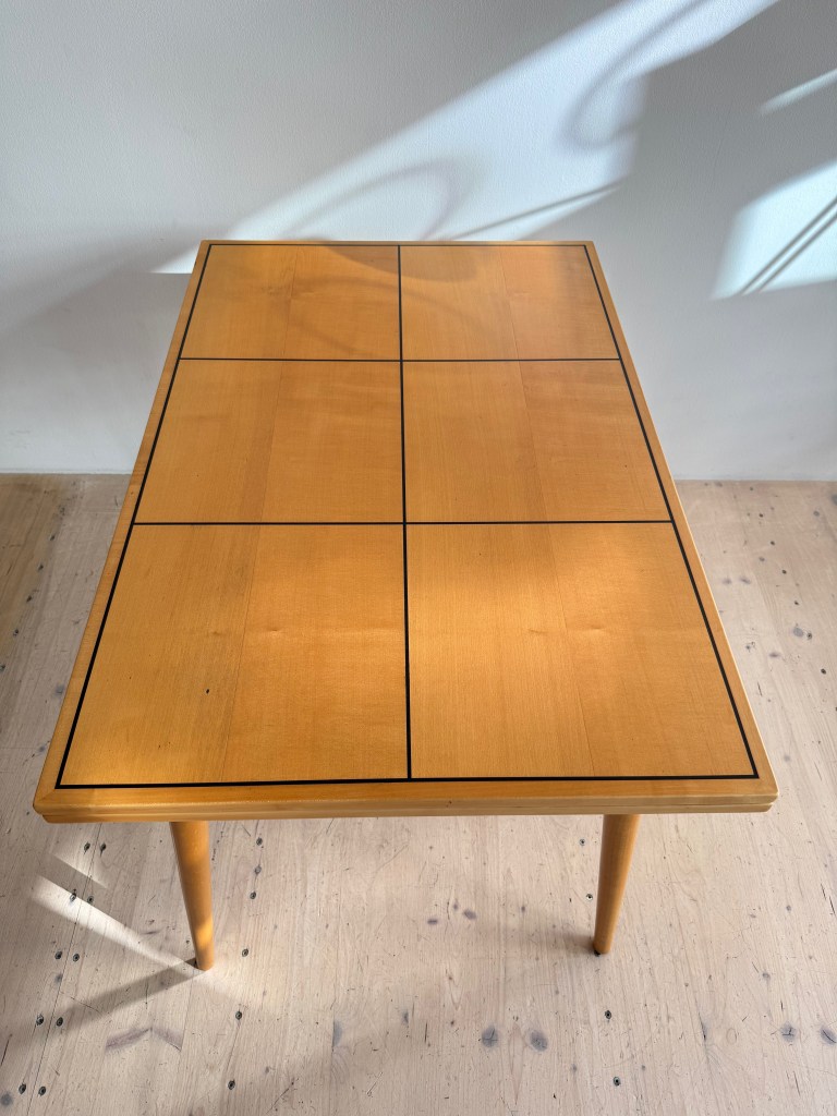 A top-down view of a wooden table with a grid pattern, featuring a light finish and black edging.