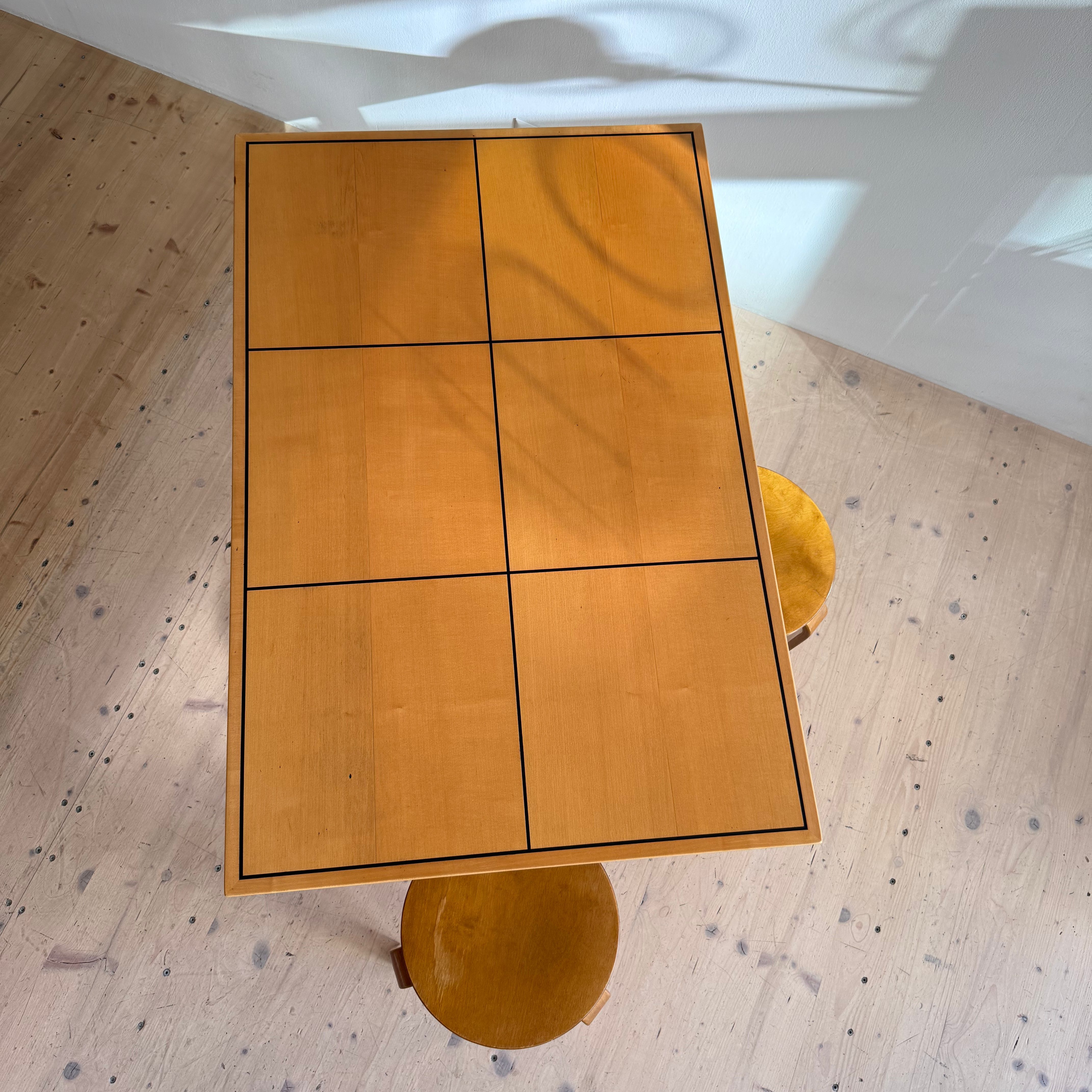 A wooden table with a grid pattern on the surface, accompanied by two round yellow stools, shot from above.