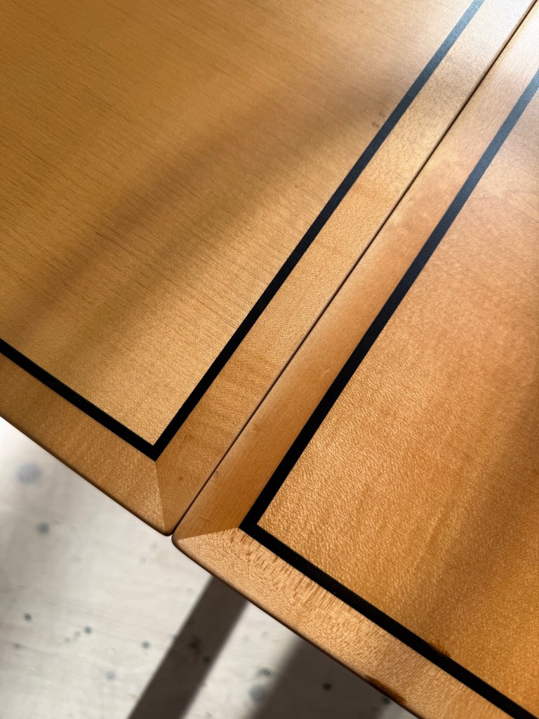 Close-up view of wooden table edges with a polished finish and contrasting black lines.