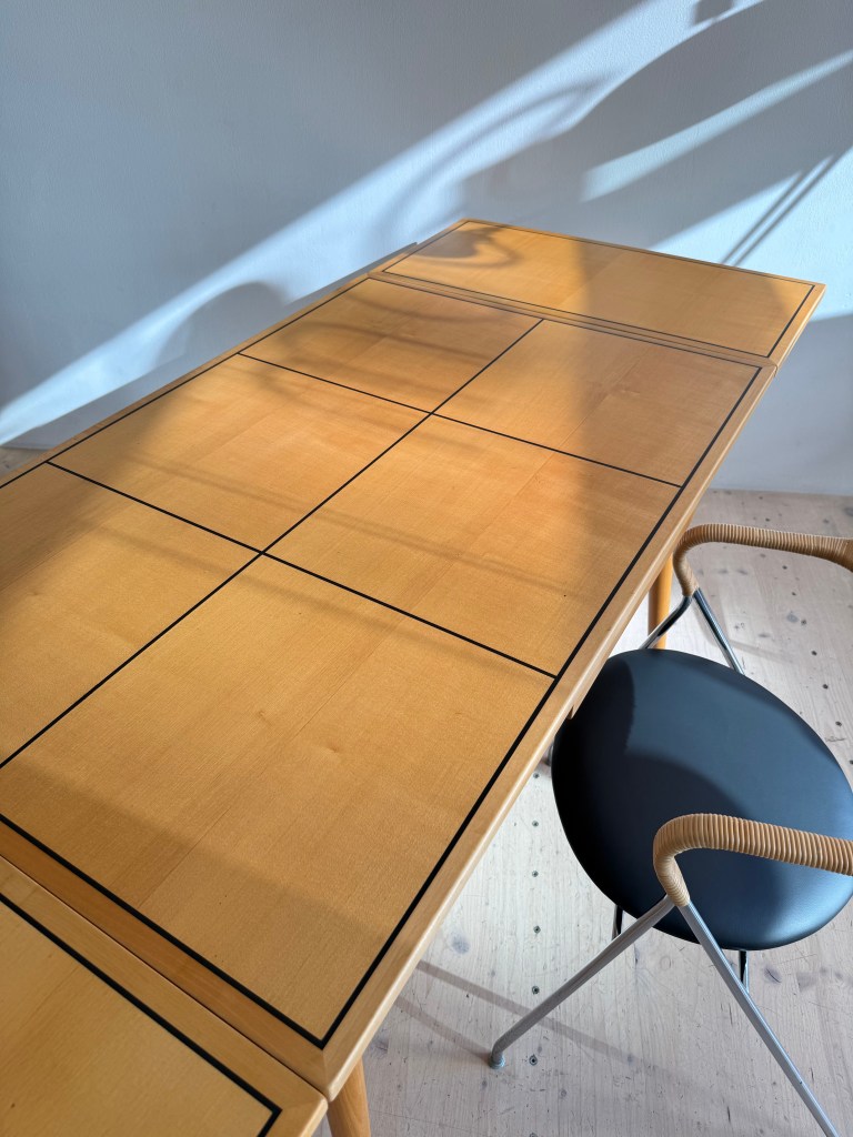 A wooden dining table with a geometric pattern on the surface, paired with a modern black chair featuring a curved seat and a rattan-back detail.