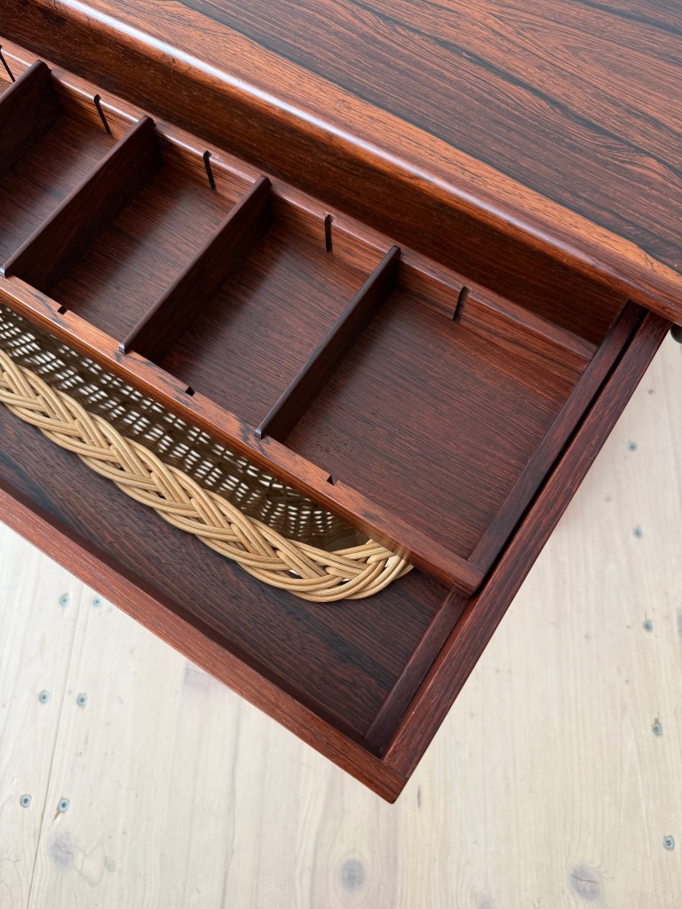 Close-up view of a wooden drawer with compartments for organization, featuring a woven basket at the bottom.