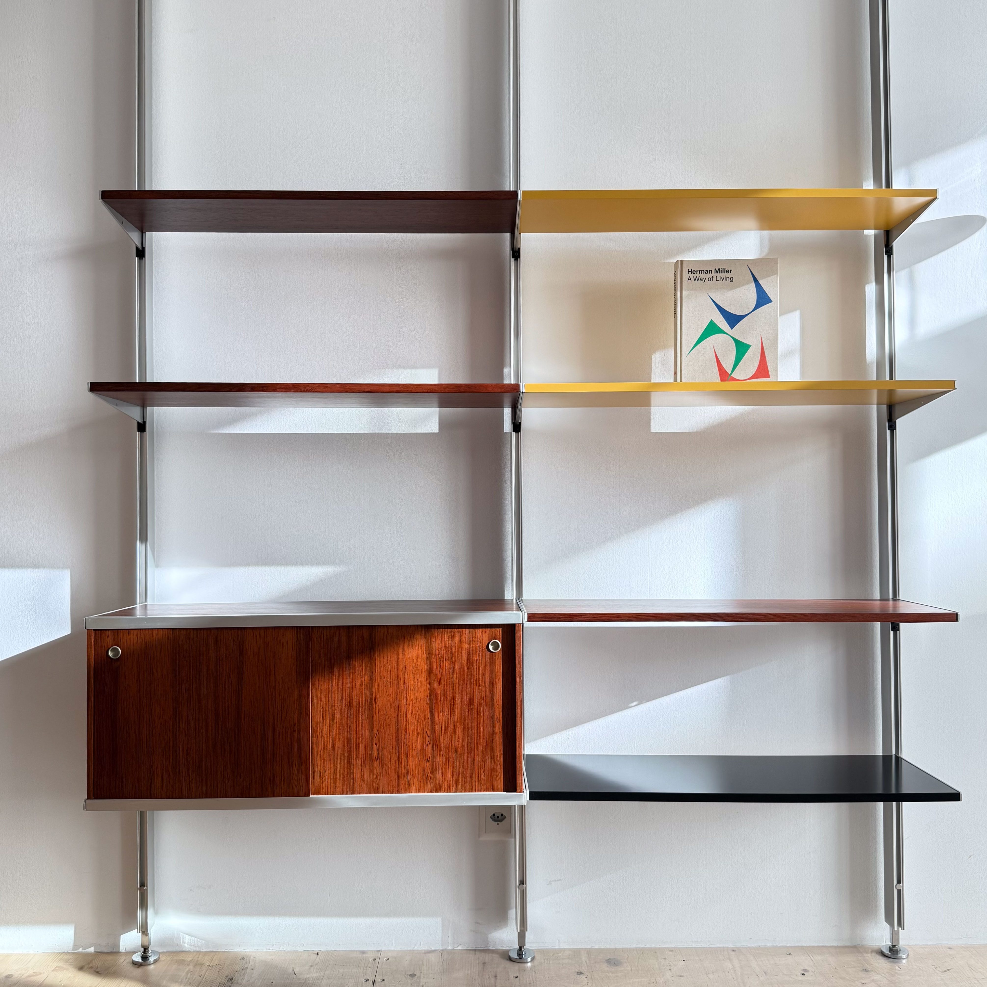 A modern shelving unit with multiple shelves in various colors, including dark wood, yellow, and black, featuring a closed storage cabinet.