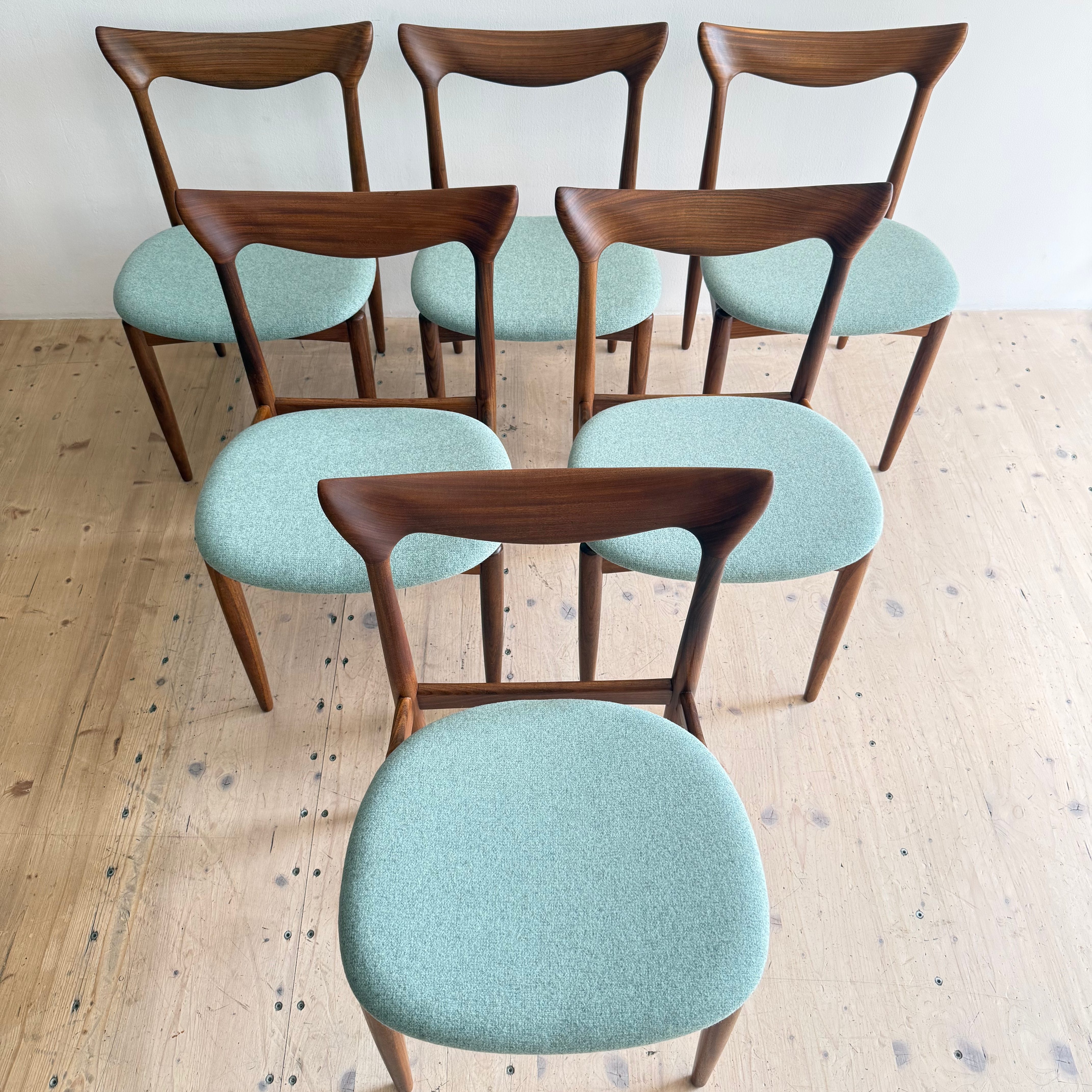 A set of six modern wooden chairs with green upholstered seats arranged in a circular pattern on a wooden floor.