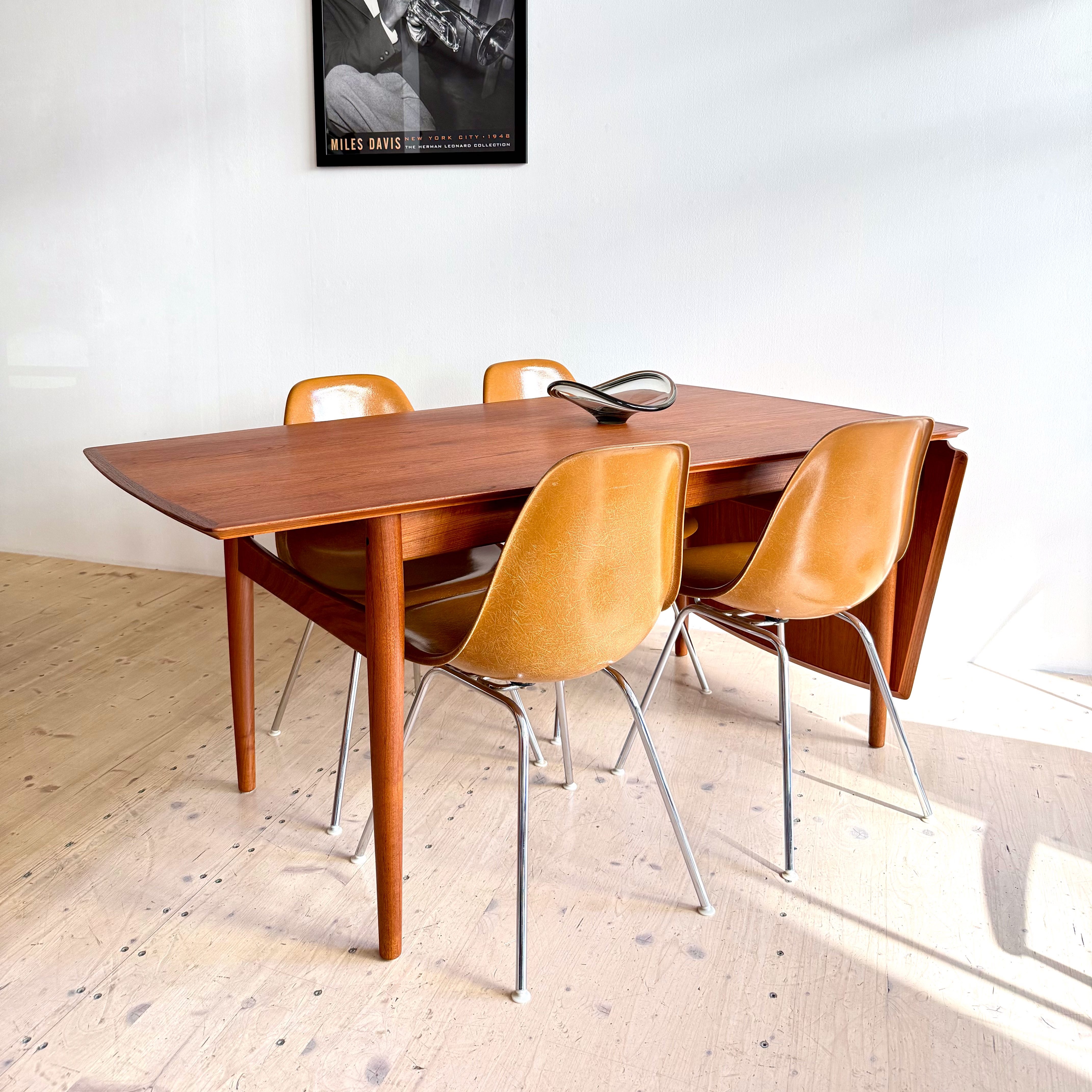 A wooden dining table surrounded by four orange chairs, with a vintage black and white poster of a musician hanging on the wall above.