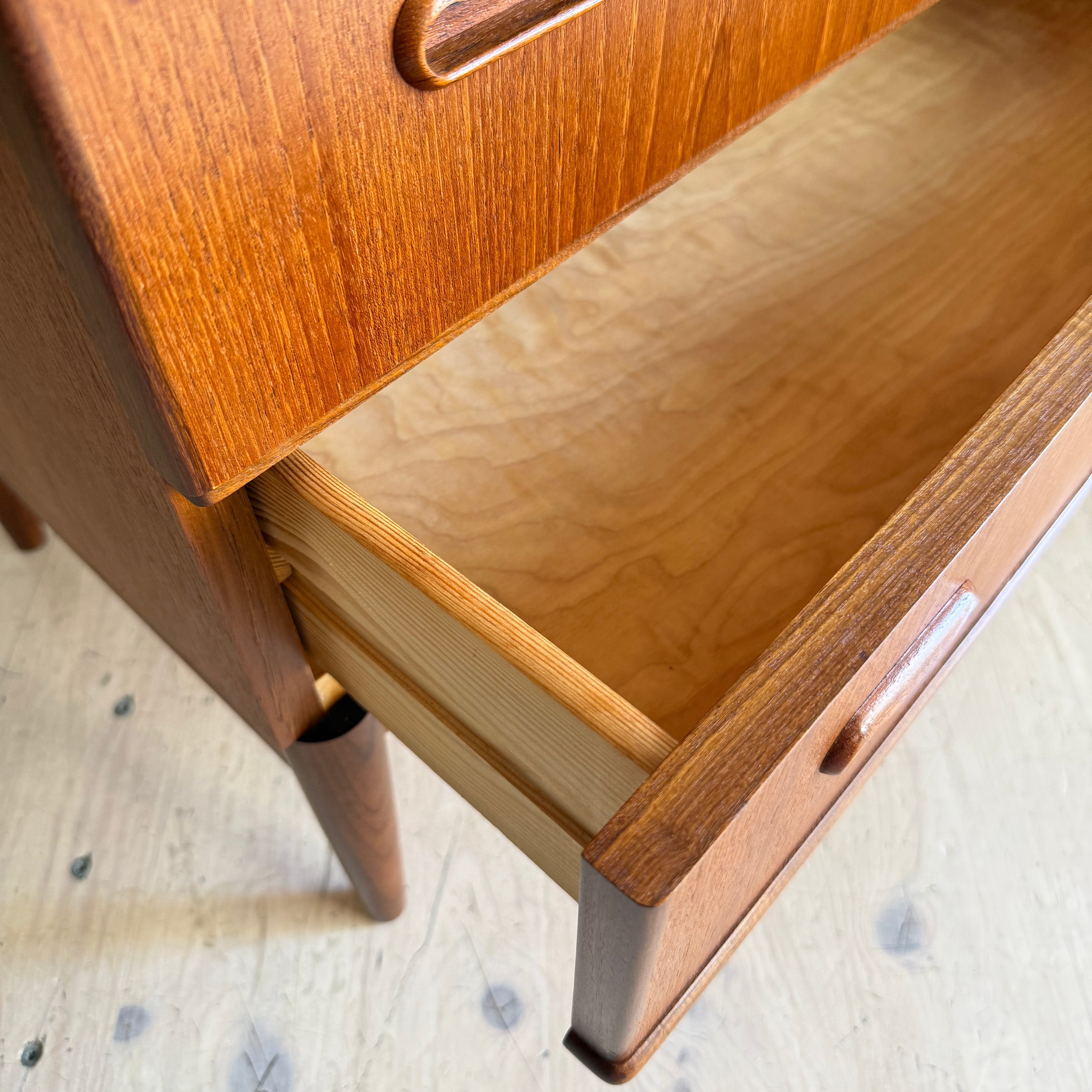 Close-up view of an open wooden drawer with a smooth, light-colored interior and a rounded wooden handle.