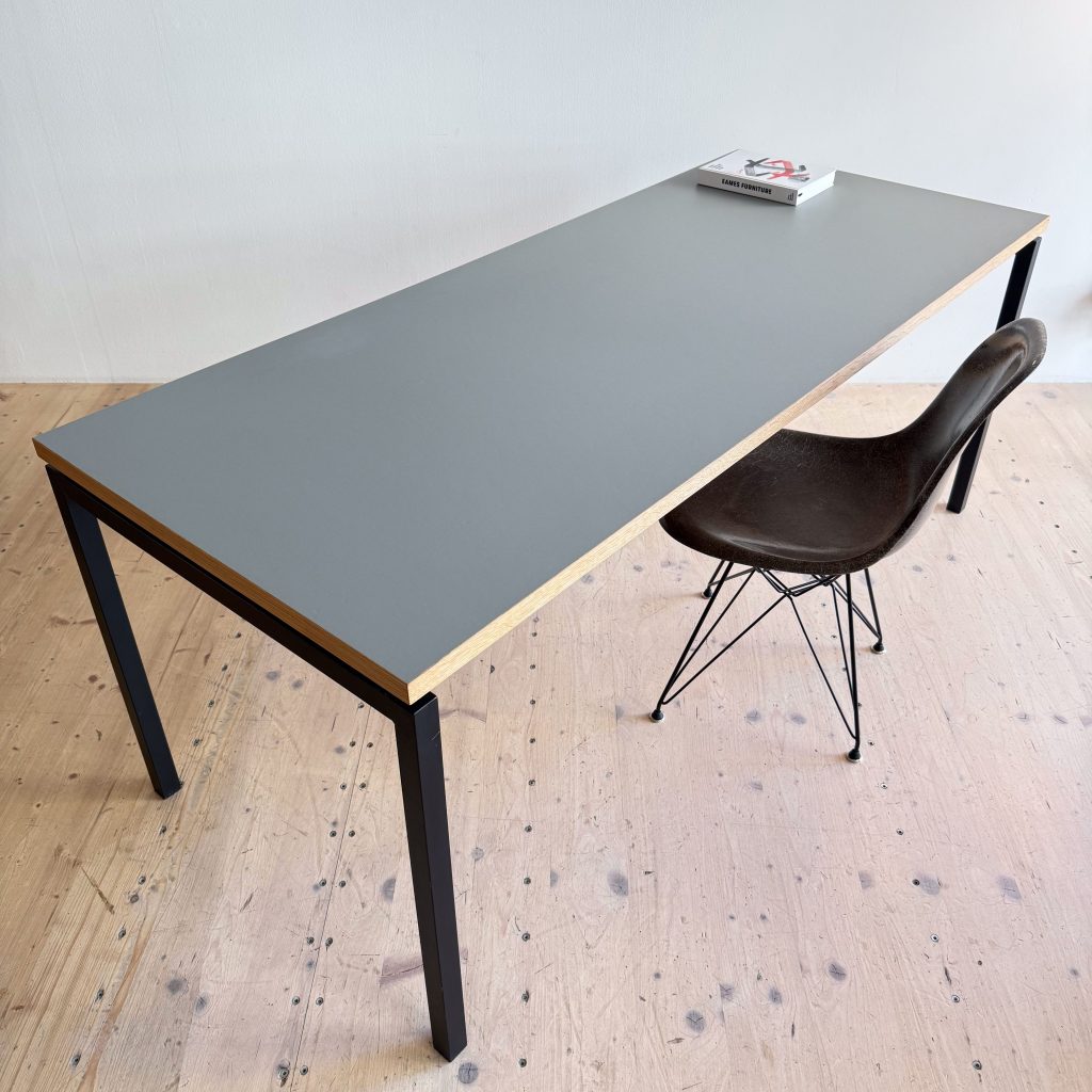 A modern, minimalist desk with a gray top and black legs, accompanied by a brown chair with metal legs, and a book placed on the table.