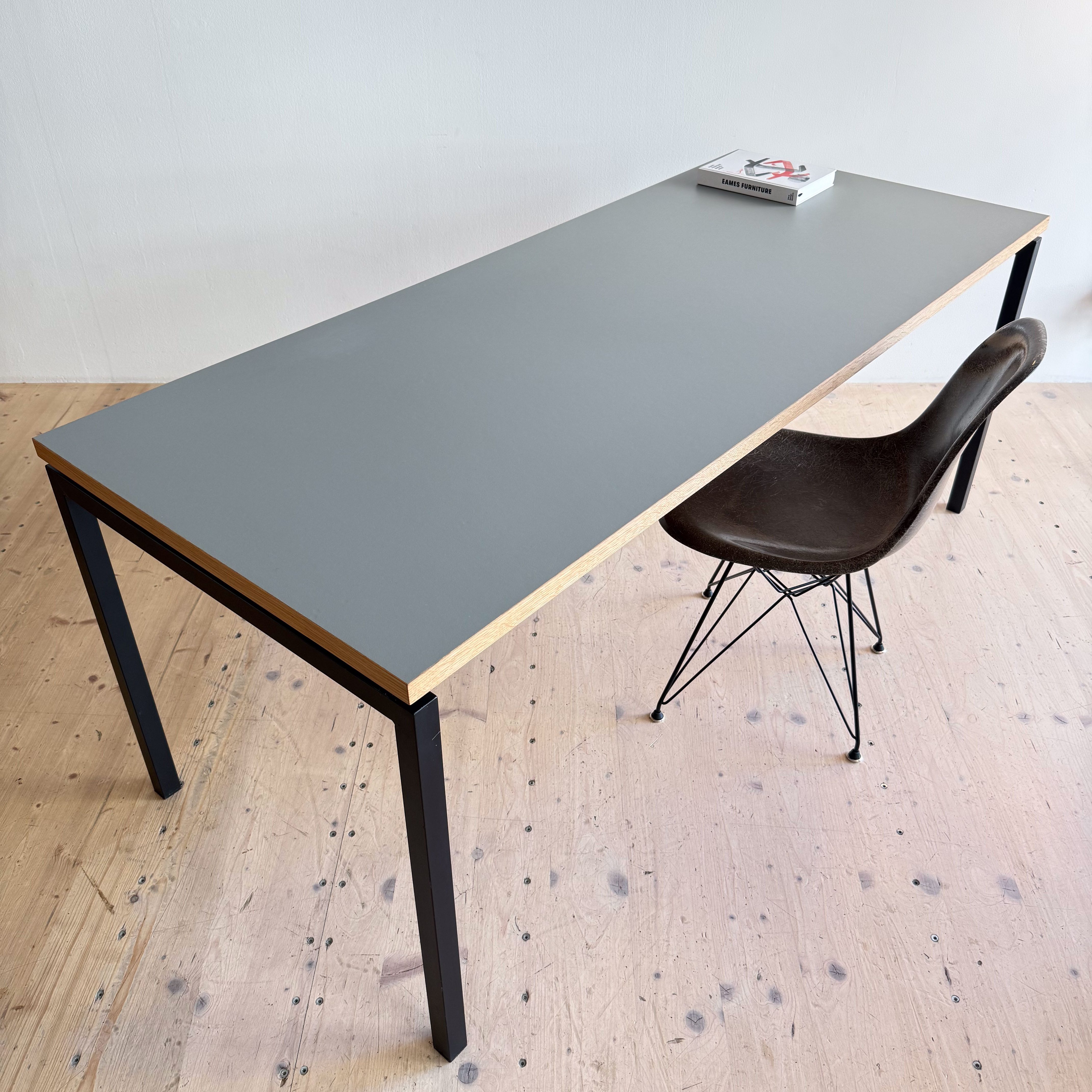 A modern grey desk with wooden edges and black metal legs, accompanied by a vintage-style chair, placed on a light wooden floor.