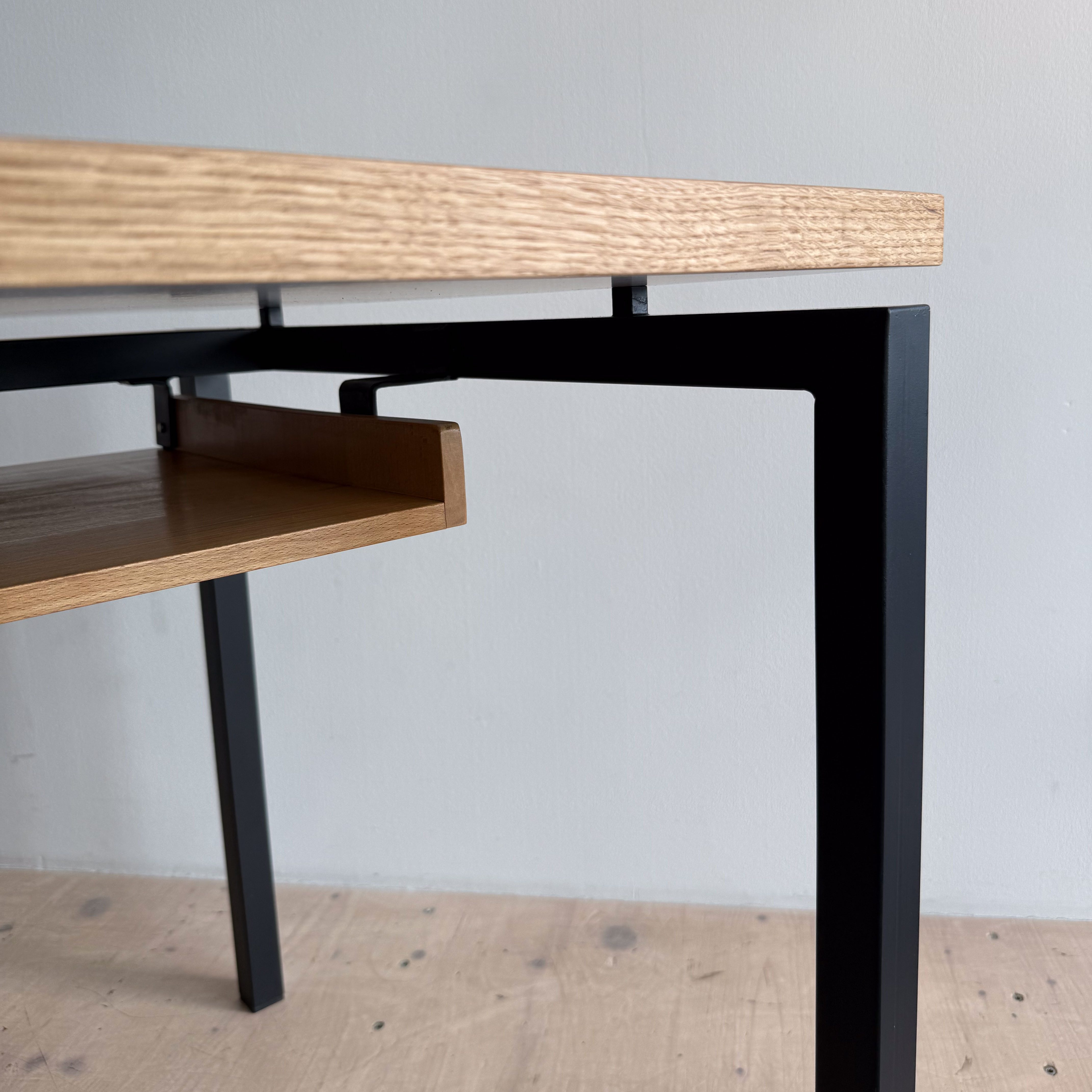 Close-up view of a modern table featuring a light wooden top and a black metal frame, showcasing a small drawer underneath.