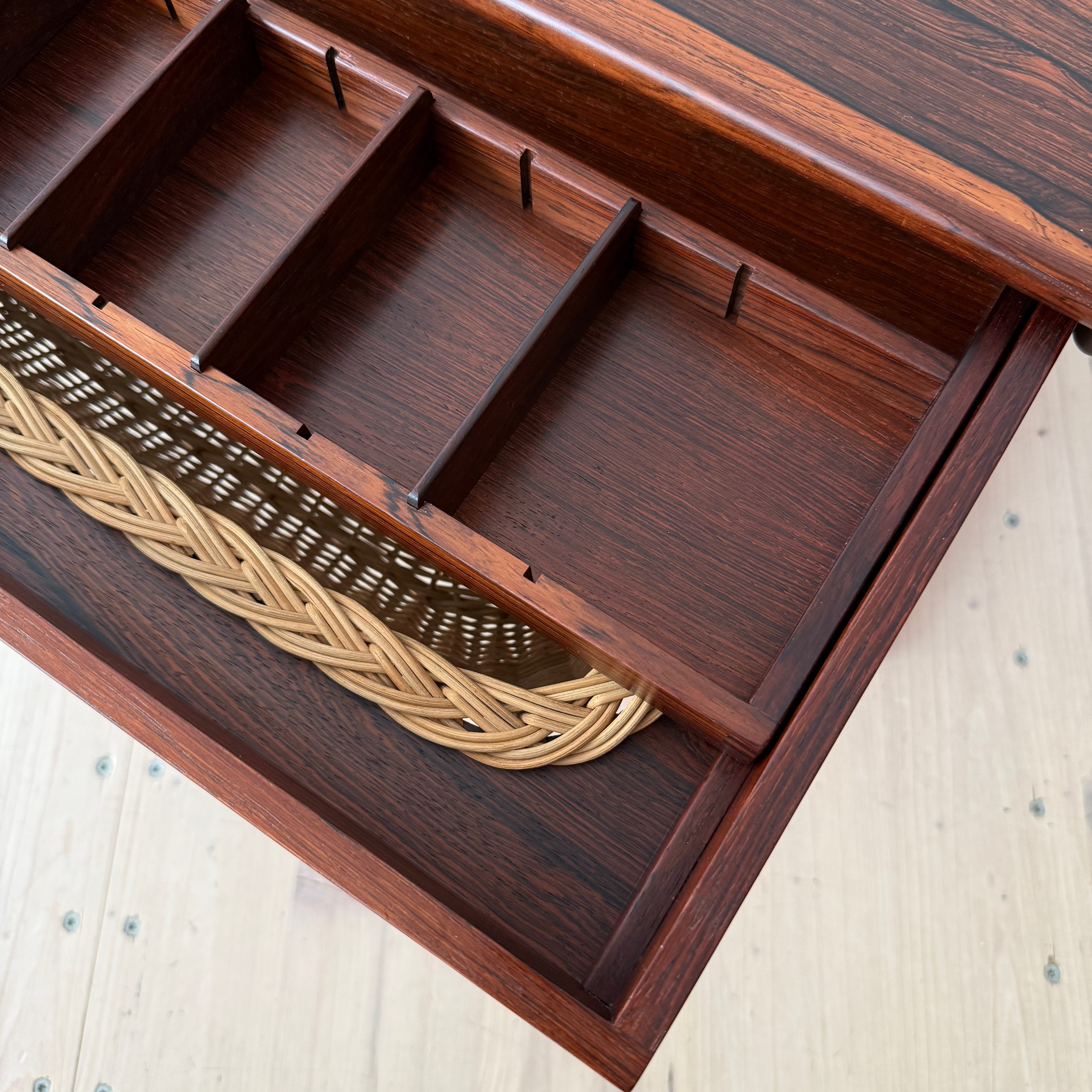 Close-up view of a wooden drawer with multiple compartments and a woven basket at the bottom.